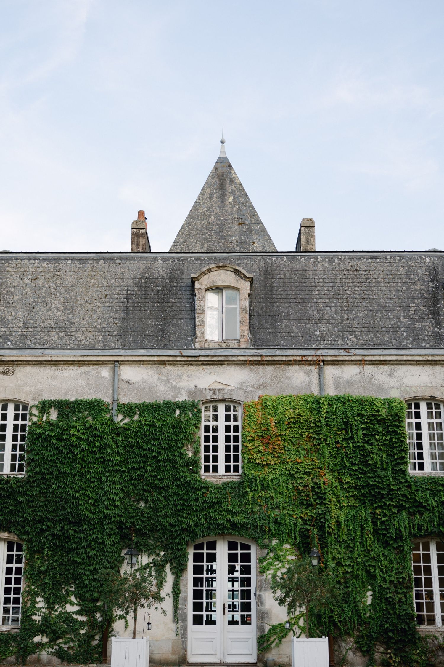 Historic French chateau covered in lush green ivy with classic mansard roof and white French doors.