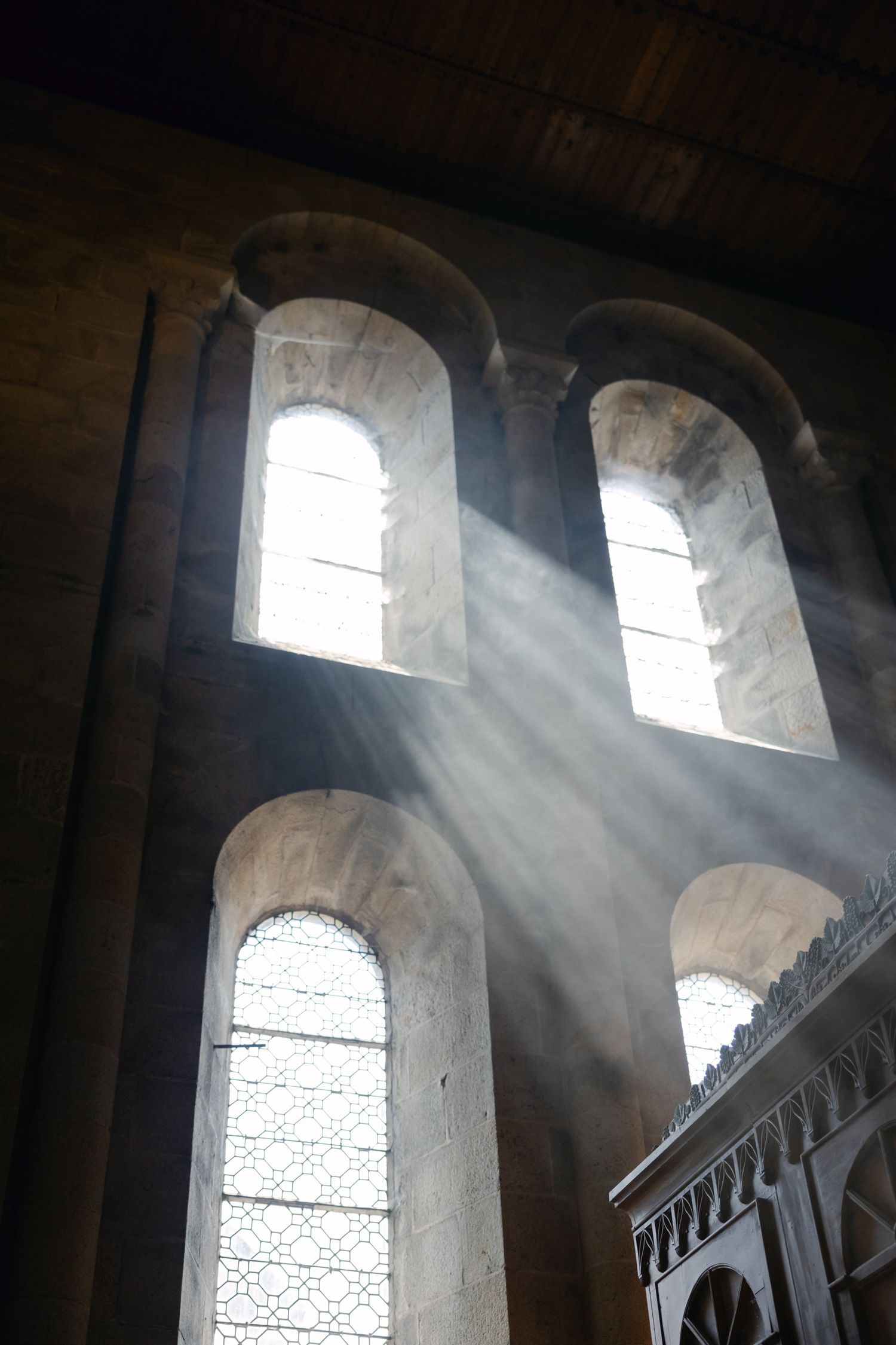 Sunlight rays streaming through arched stone windows in a historic cathedral, illuminating the dark interior with dramatic light beams.