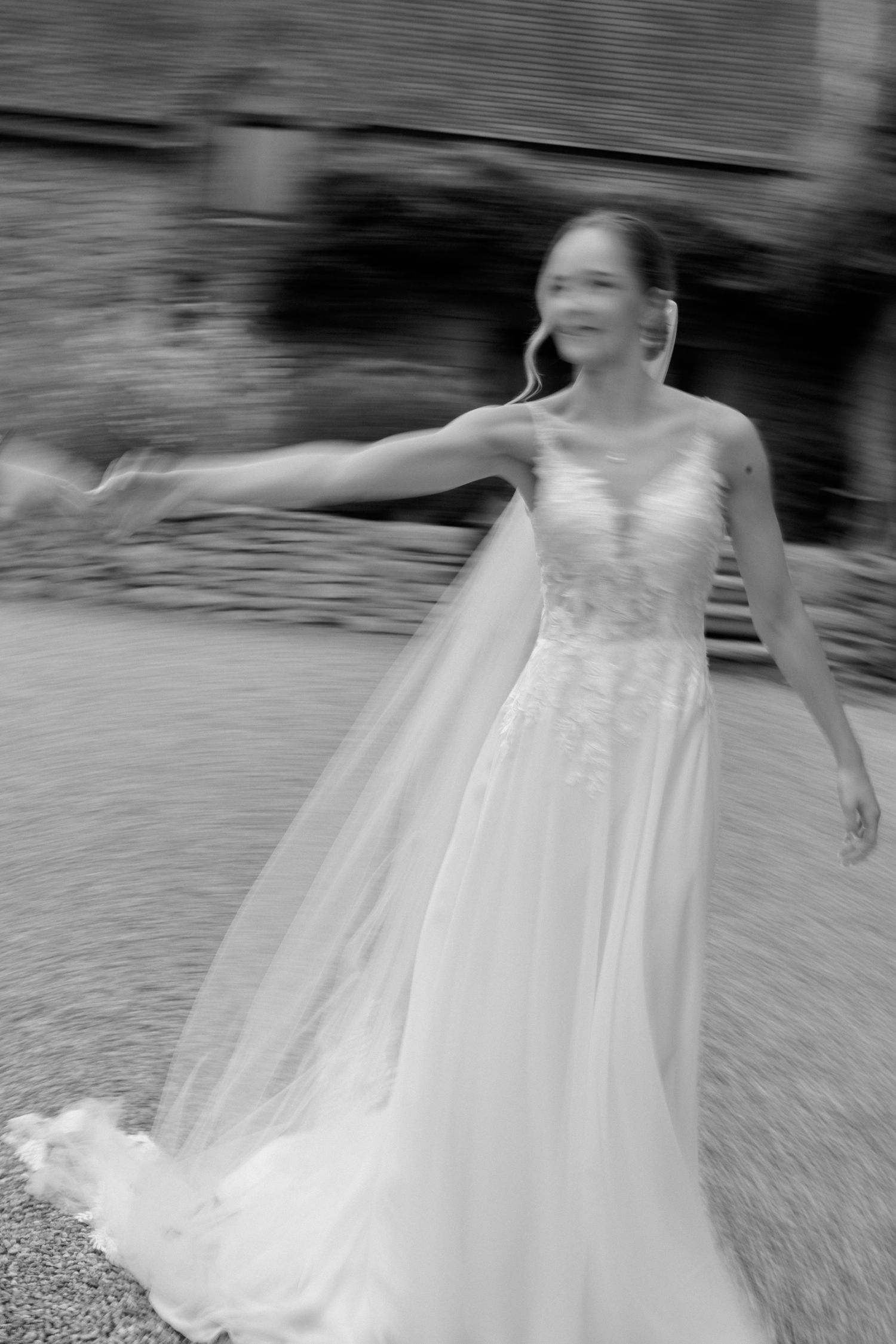 Photo en noir et blanc d'une joyeuse mariée qui tourne dans une robe de mariée en dentelle avec un voile fluide.