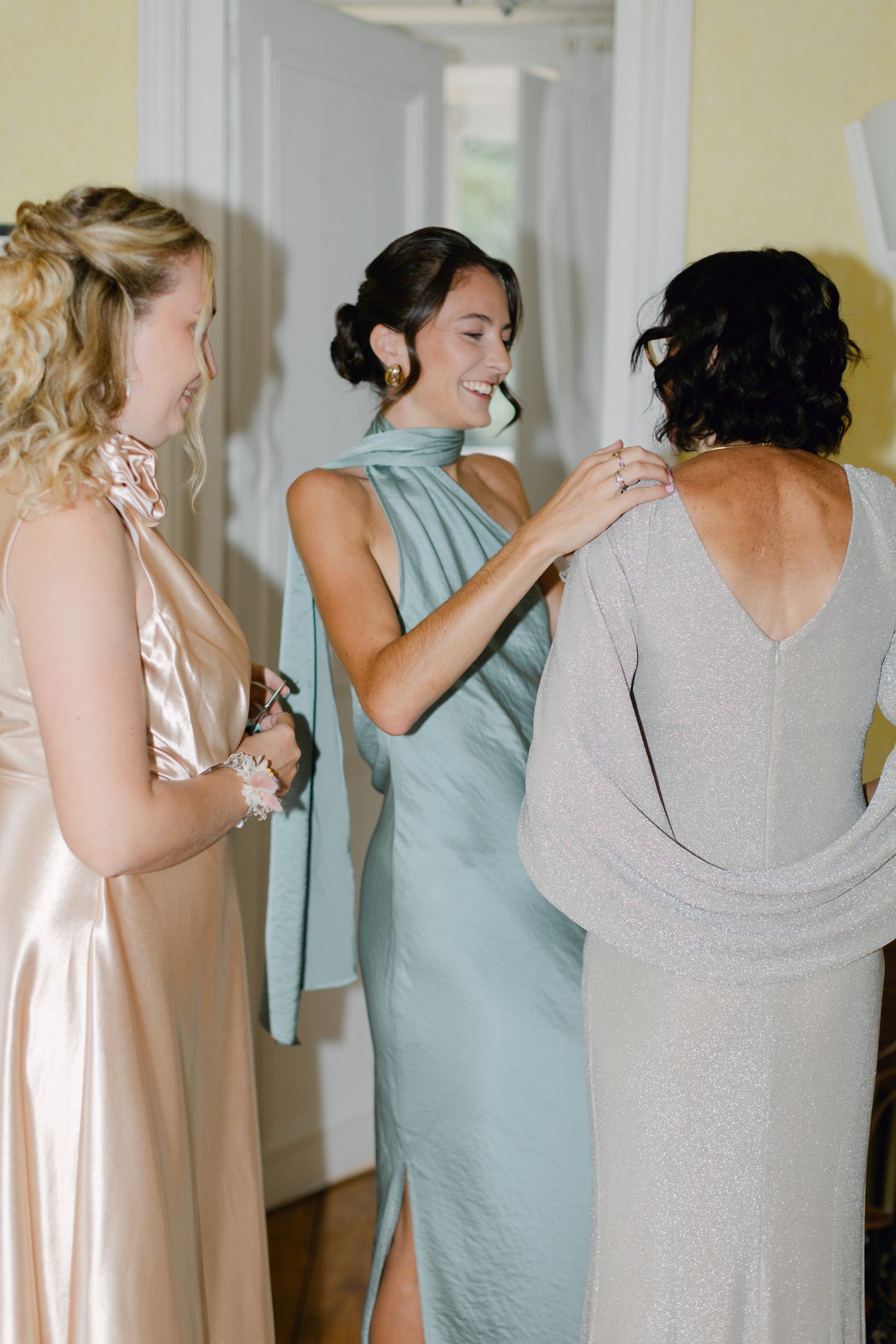 Des demoiselles d'honneur en robes de satin s'entraident à se préparer avant la cérémonie de mariage.
