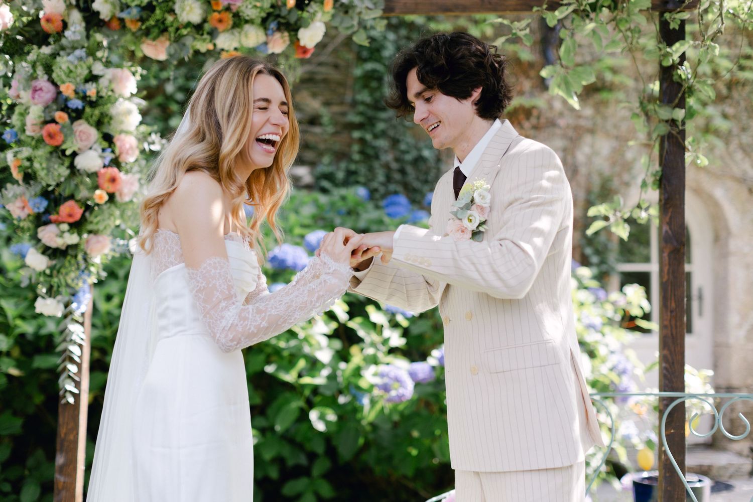 La mariée rit joyeusement alors que le marié place l'alliance à son doigt lors d'une cérémonie en plein air.