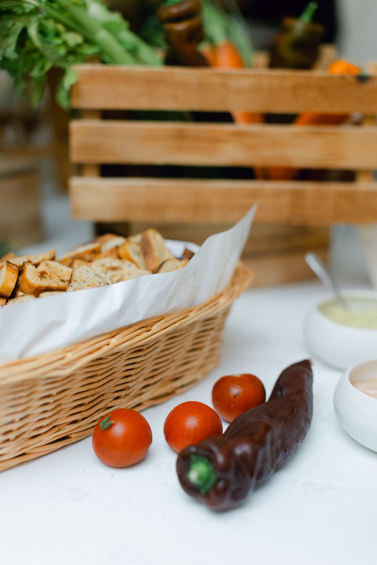 Panier à pain rustique en osier avec tomates cerises et poivron noir sur un présentoir de table blanc.