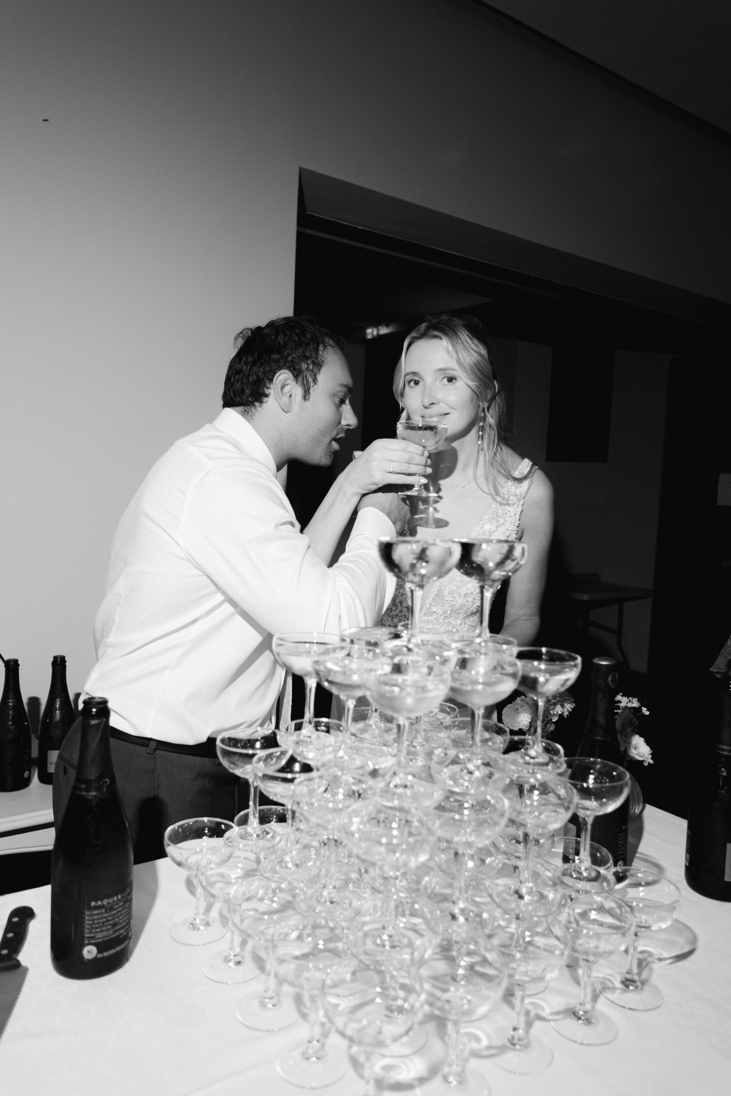La mariée et le marié grillent du champagne à côté d'une élégante tour de verre coupé lors d'une réception de mariage en noir et blanc.