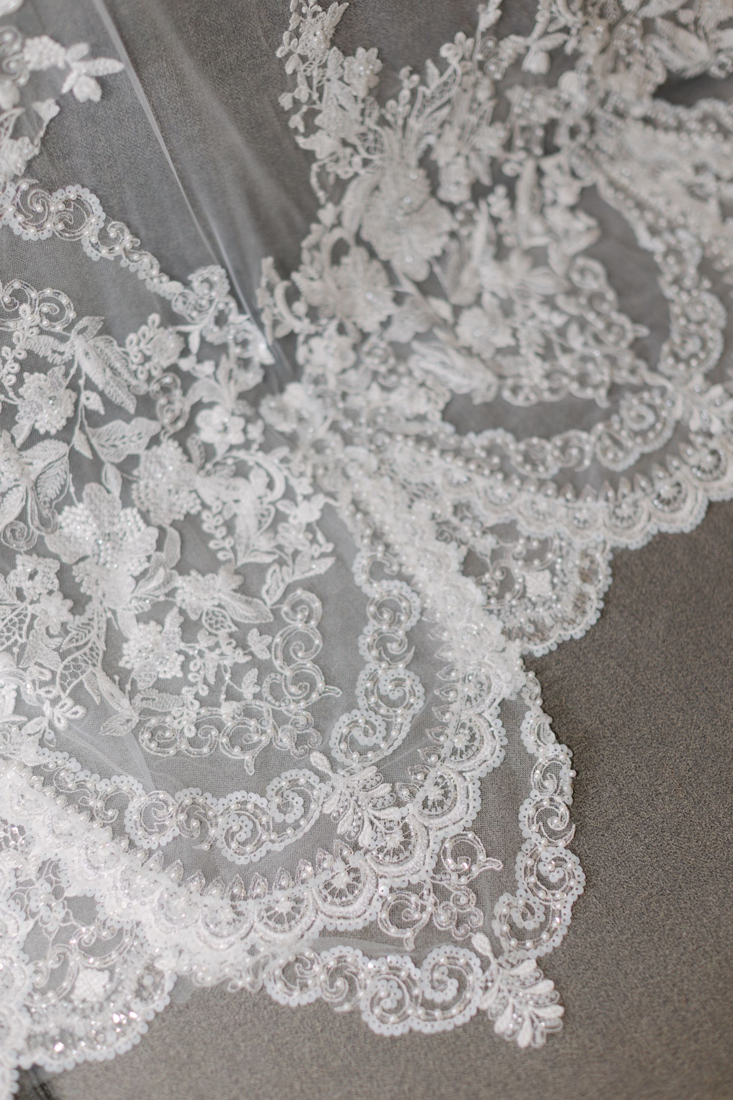 Gros plan d'une broderie de dentelle florale complexe sur un voile de mariage blanc avec des détails perlés.