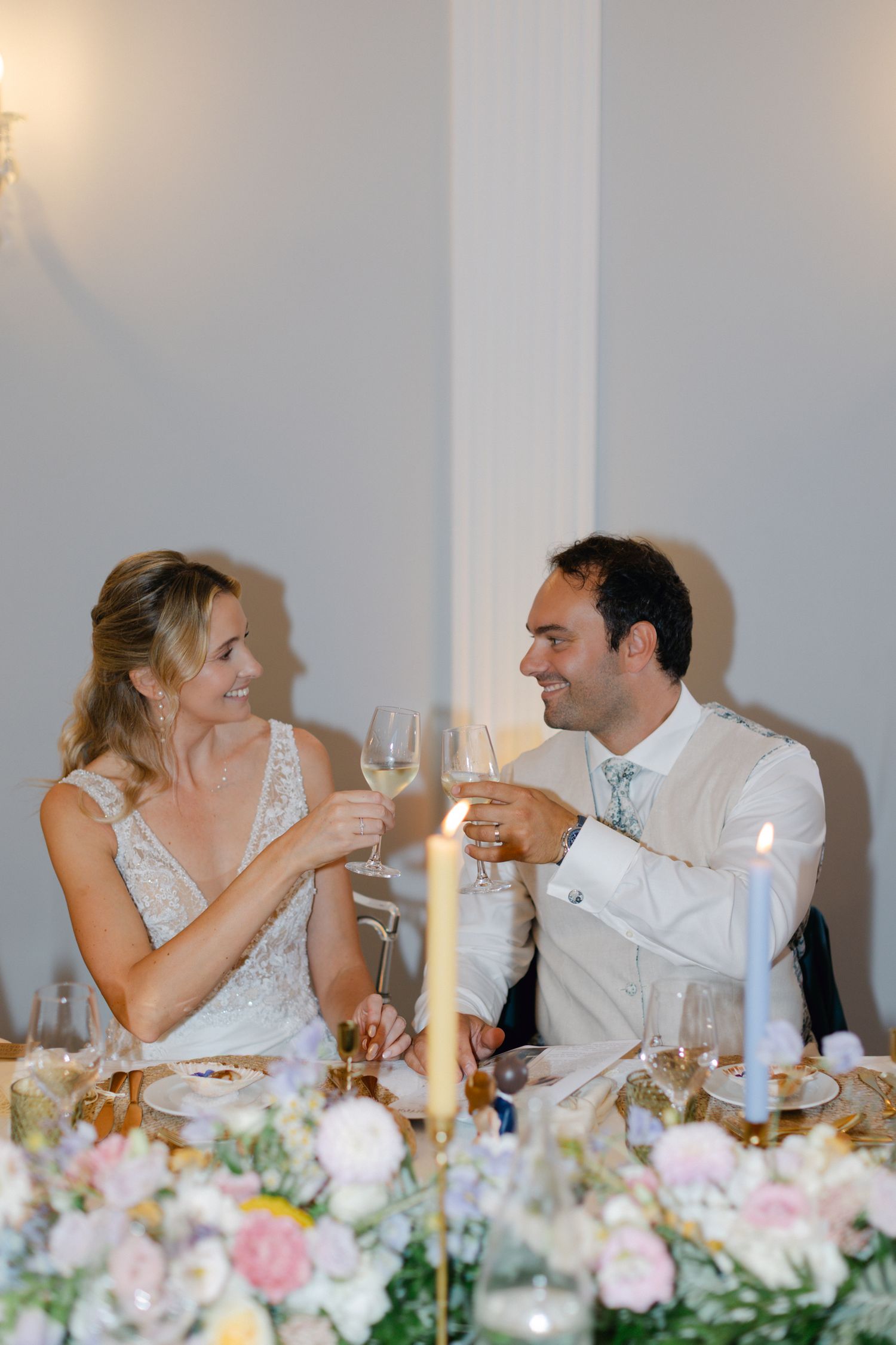 La mariée et le marié trinquent avec des verres à vin à la table de réception de mariage décorée de fleurs.