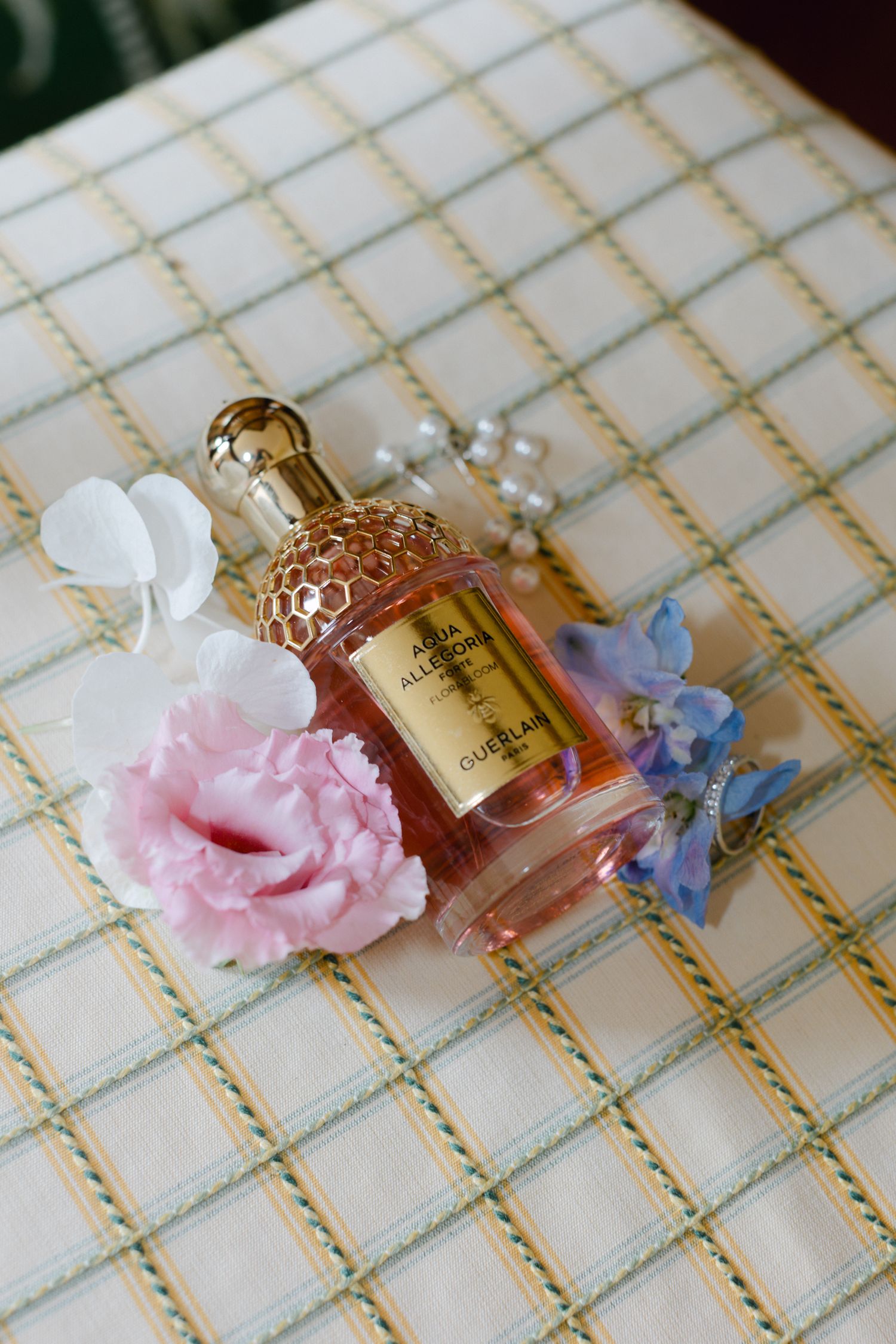 Bouteille de parfum Guerlain Aqua Allegoria entourée de fleurs roses et bleues avec des bijoux en perles.