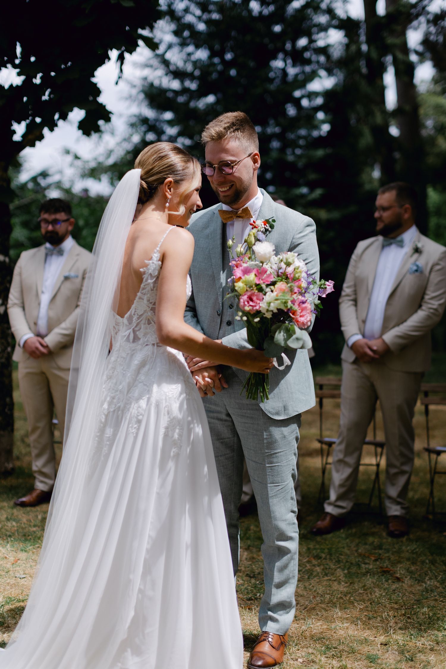 La mariée et le marié partagent un moment émouvant tenant un bouquet coloré lors de la cérémonie de mariage en plein air.