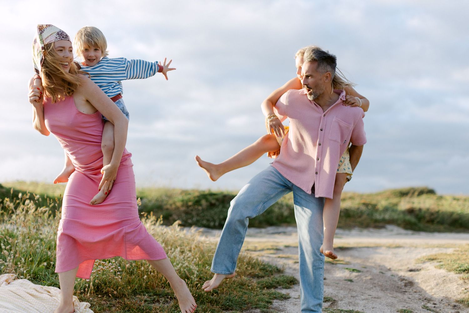 Famille heureuse jouant sur une plage de sable, les parents font des promenades à cheval aux enfants par une journée nuageuse.