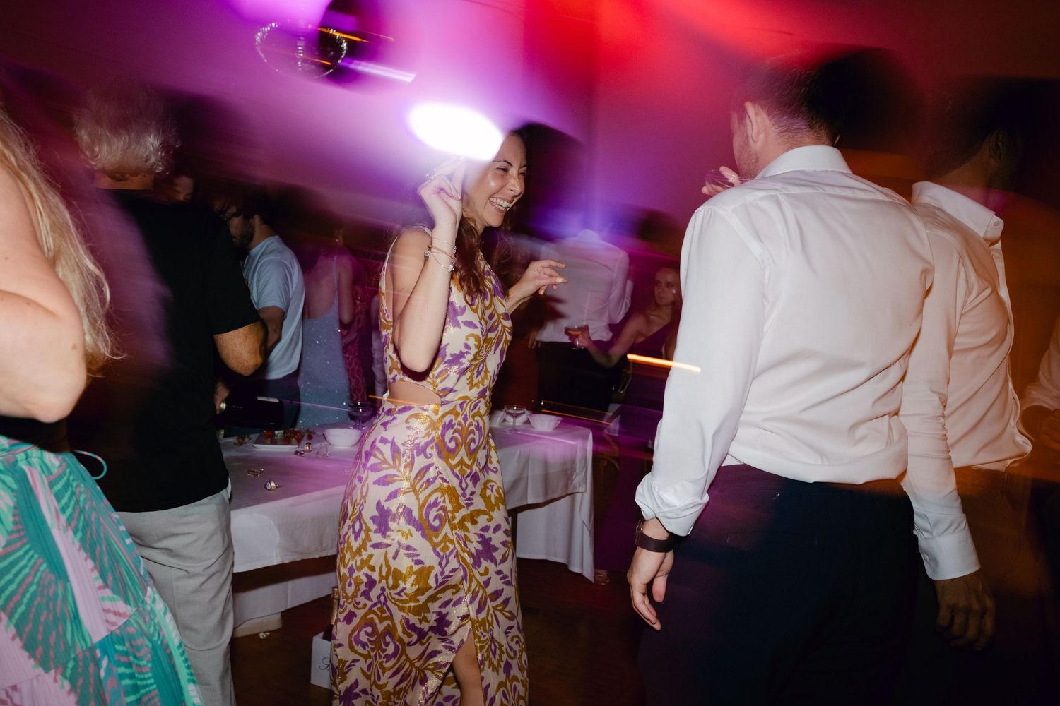 Invité en robe florale dansant sous des lumières colorées lors d'une réception de mariage animée.