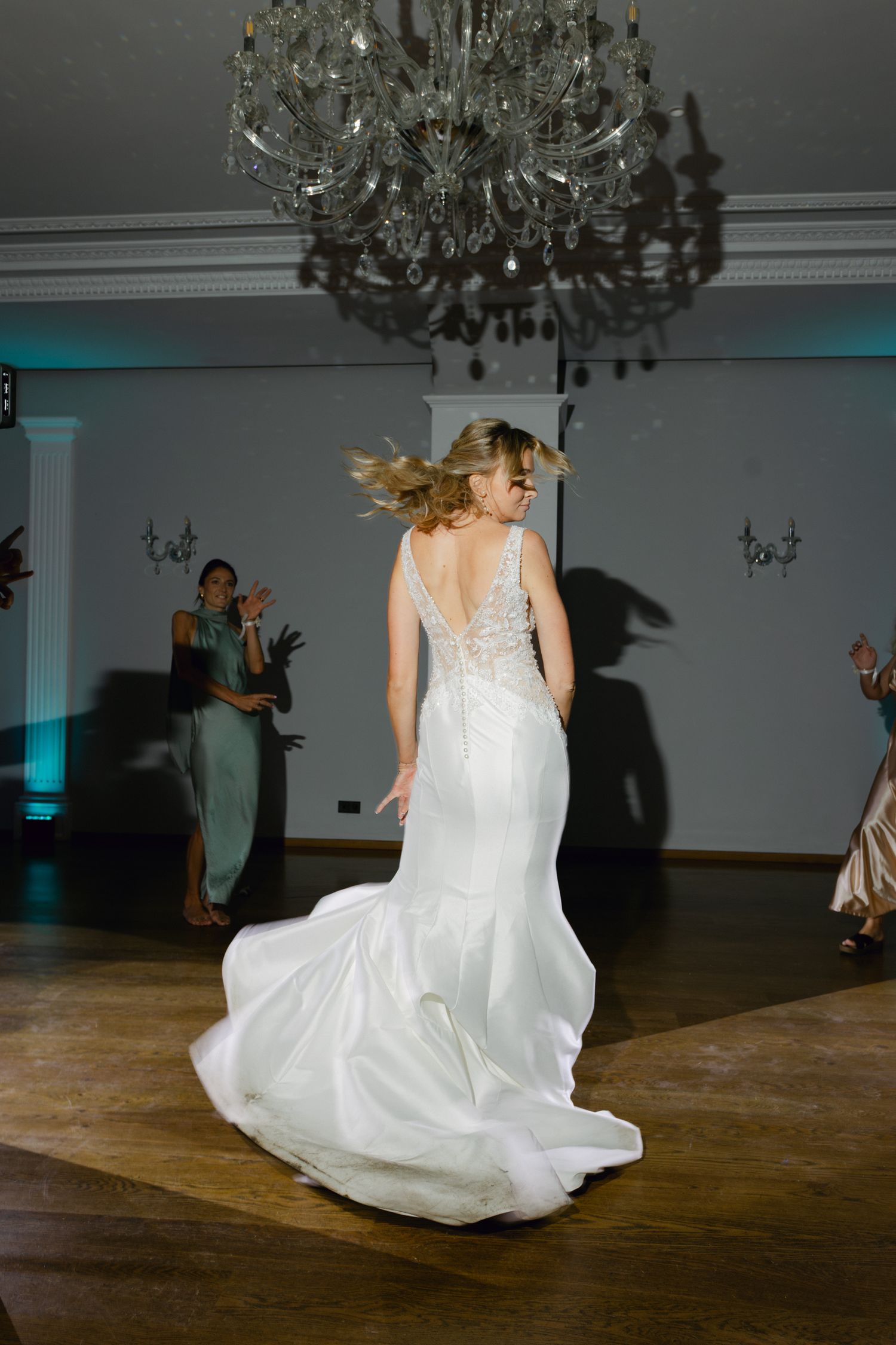 Mariée en robe en dentelle ajustée tourbillonnant sous un lustre en cristal sur la piste de danse lors d'une élégante réception de mariage.