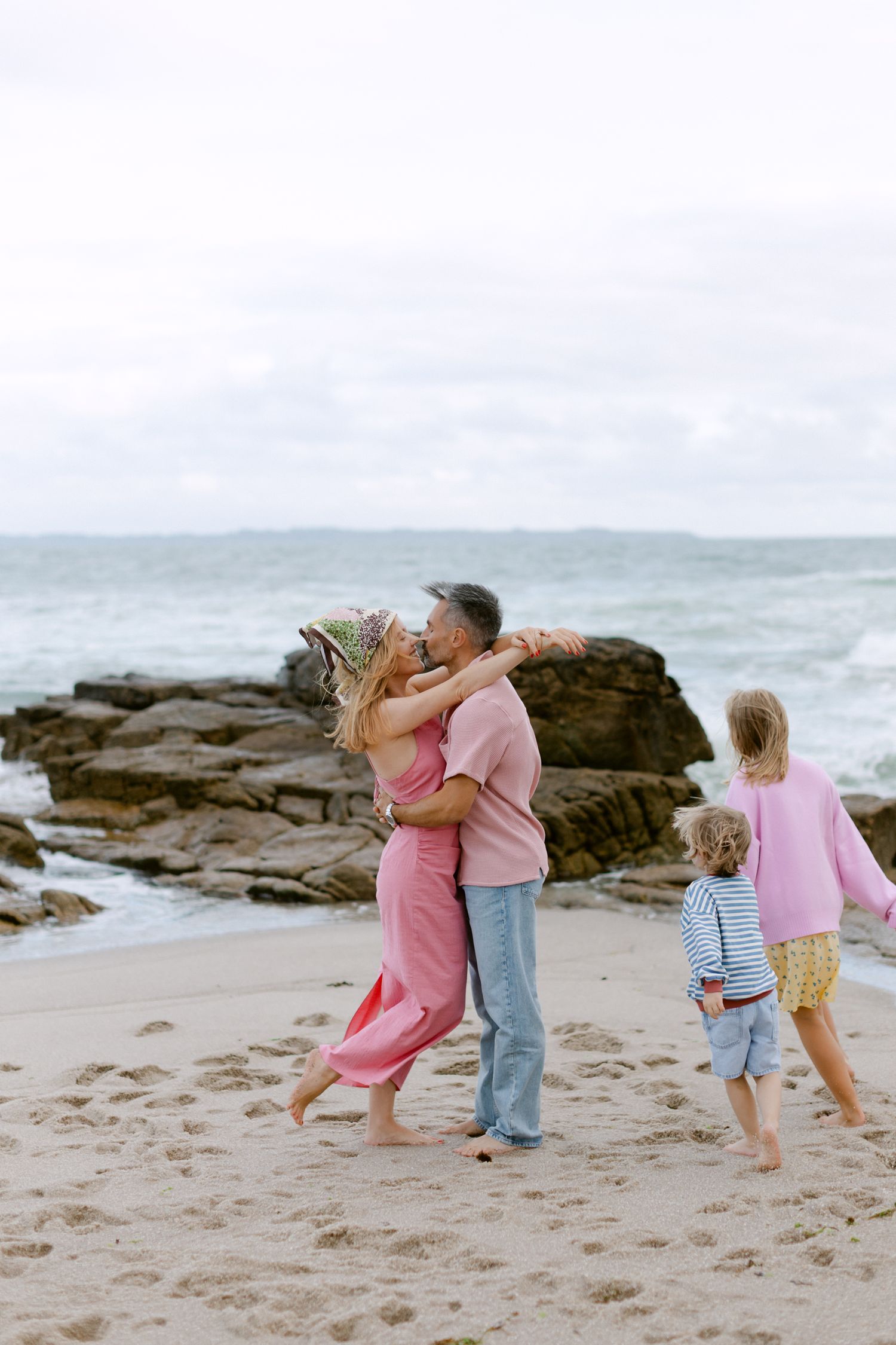 Un couple s'embrasse et s'embrasse sur une plage de sable pendant que deux jeunes enfants jouent à proximité avec les vagues de l'océan.