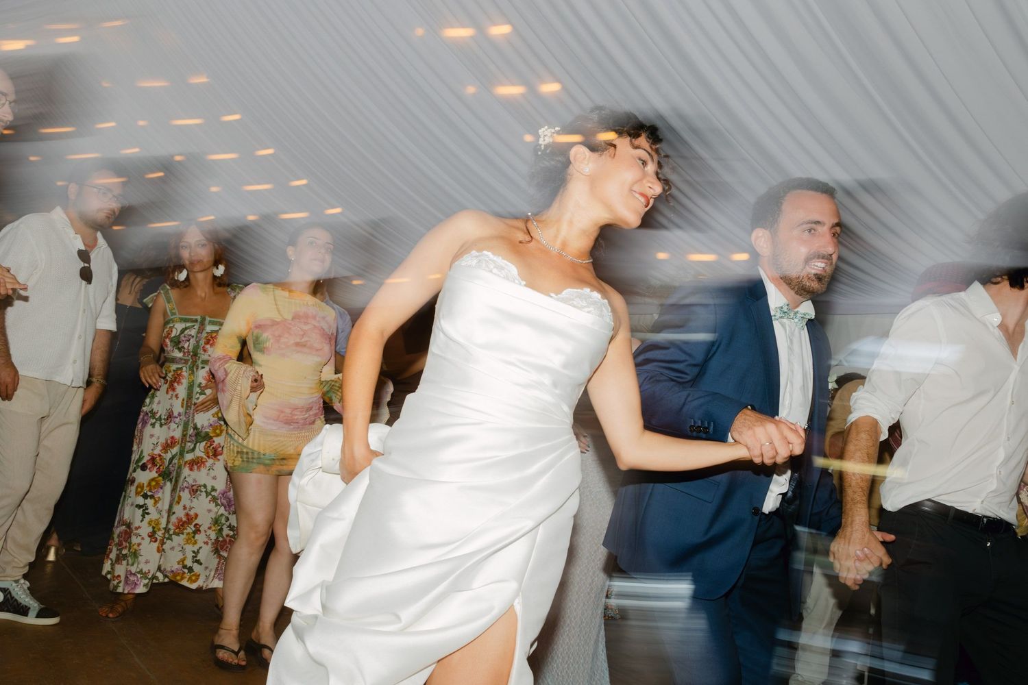 Bride in white gown dancing energetically with guests at a wedding reception celebration.