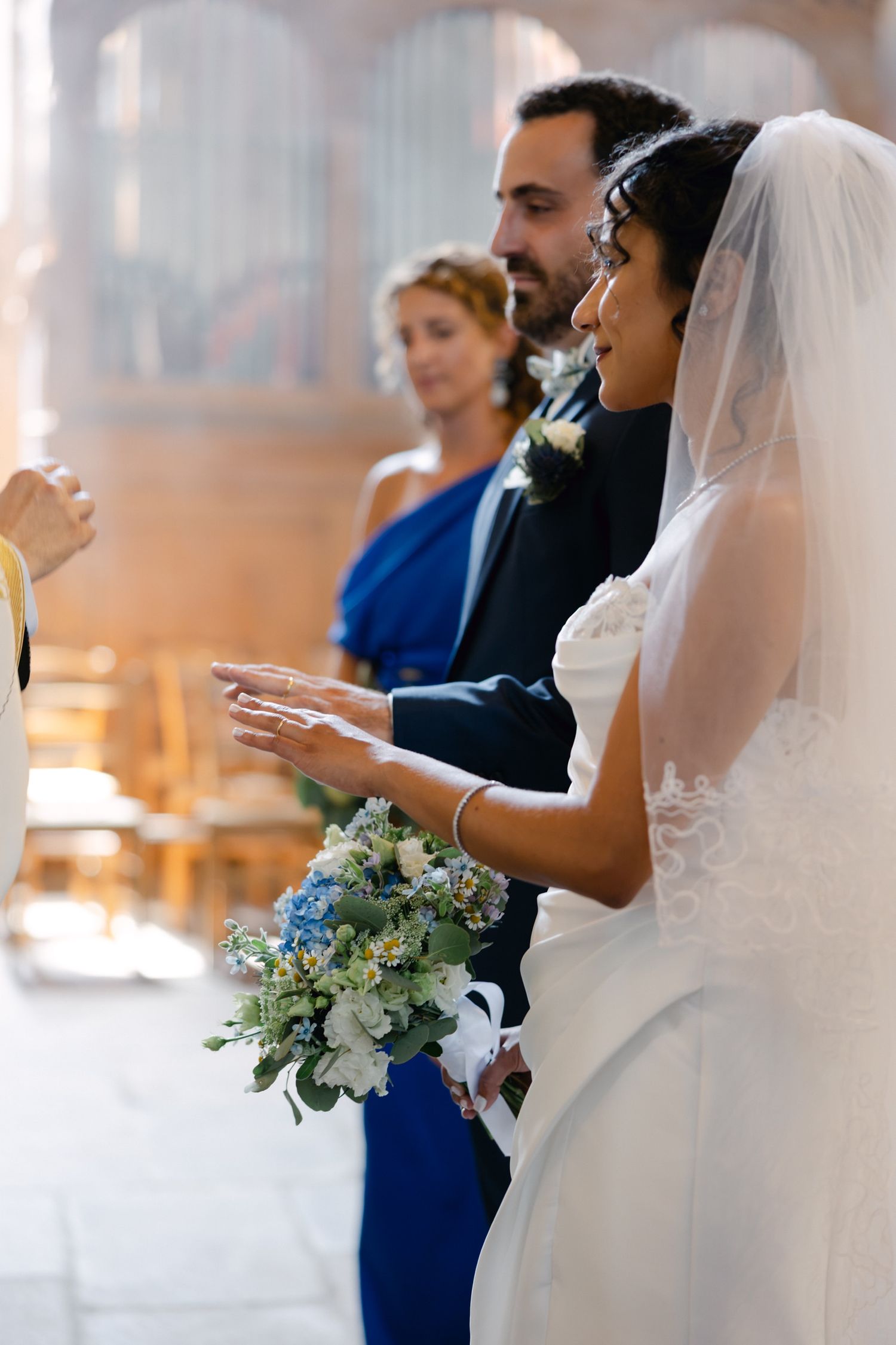 Bride holding blue and white bouquet with groom during wedding ceremony in church.