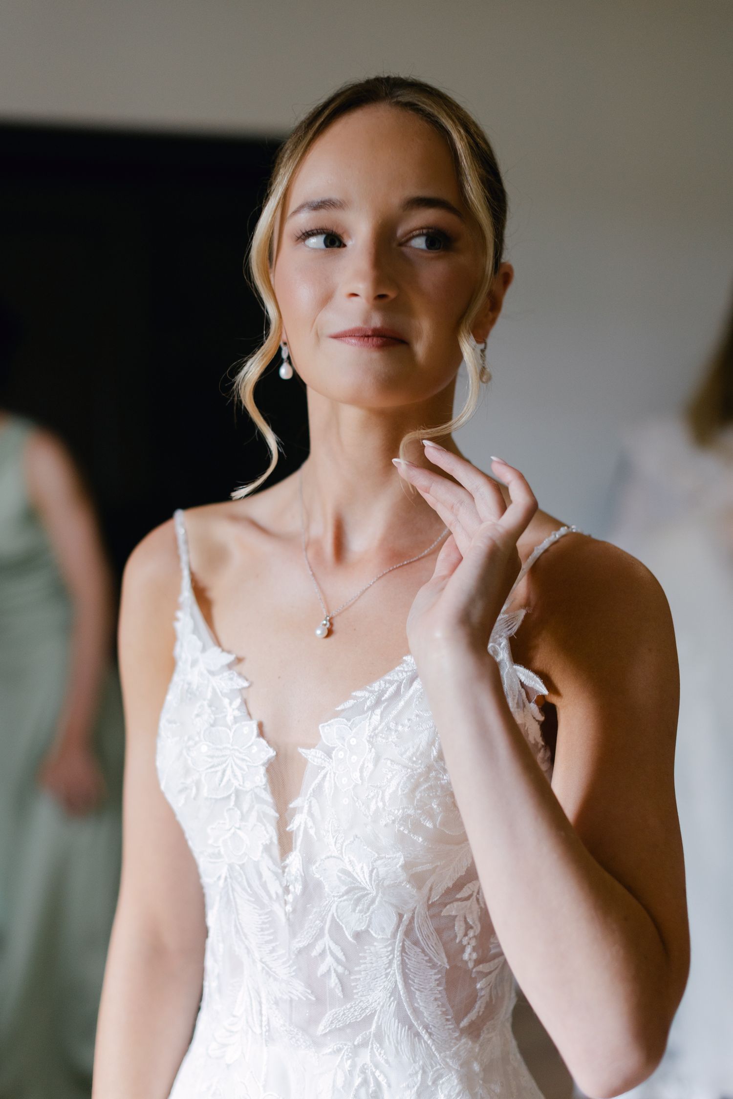 Belle mariée en robe de mariée en dentelle florale ajustant le collier de perles pendant la préparation de la mariée.
