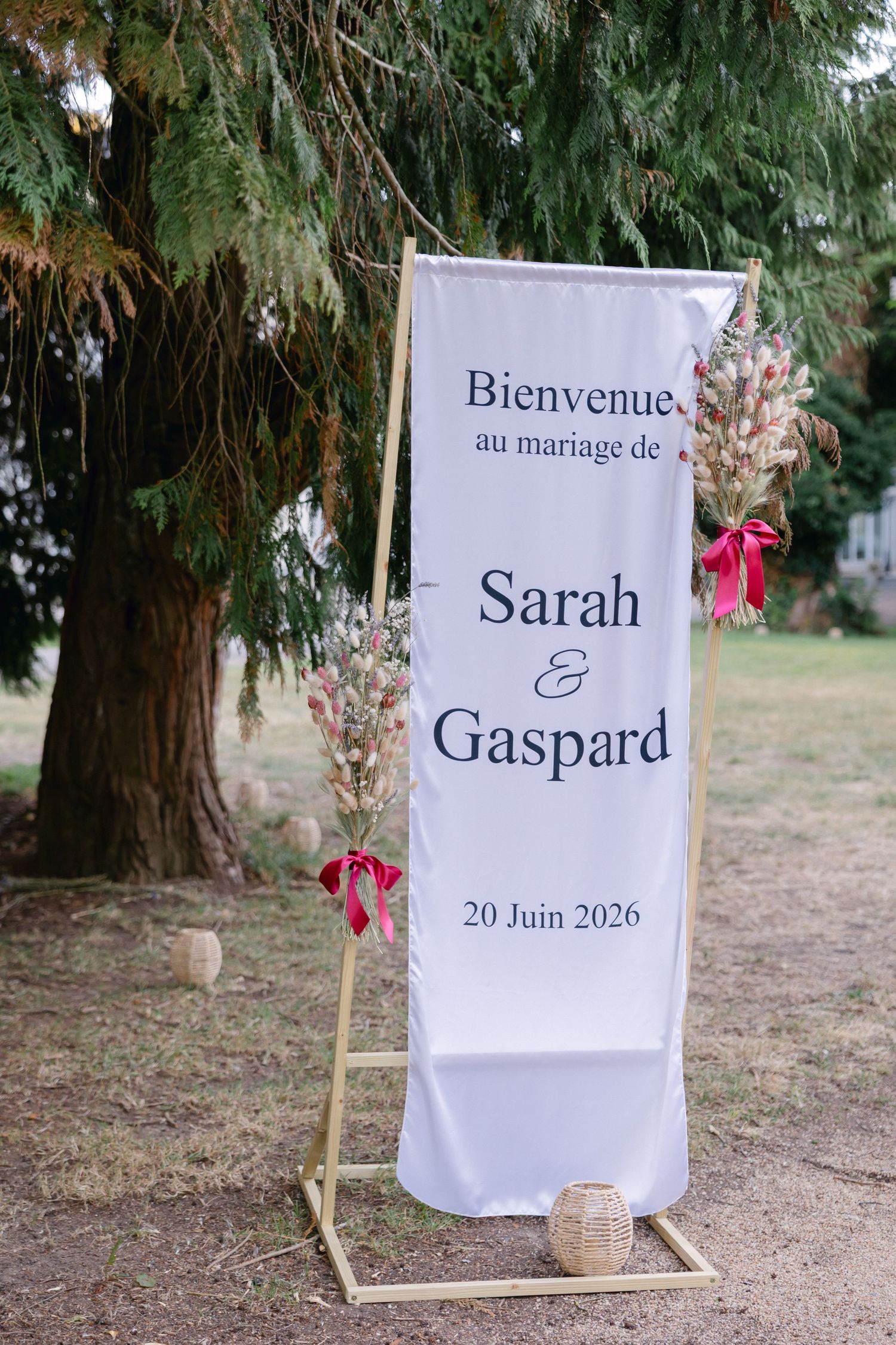 Panneau de bienvenue de mariage en plein air en français pour Sarah et Gaspard, daté du 20 juin 2026, décoré de fleurs de ruban rose.