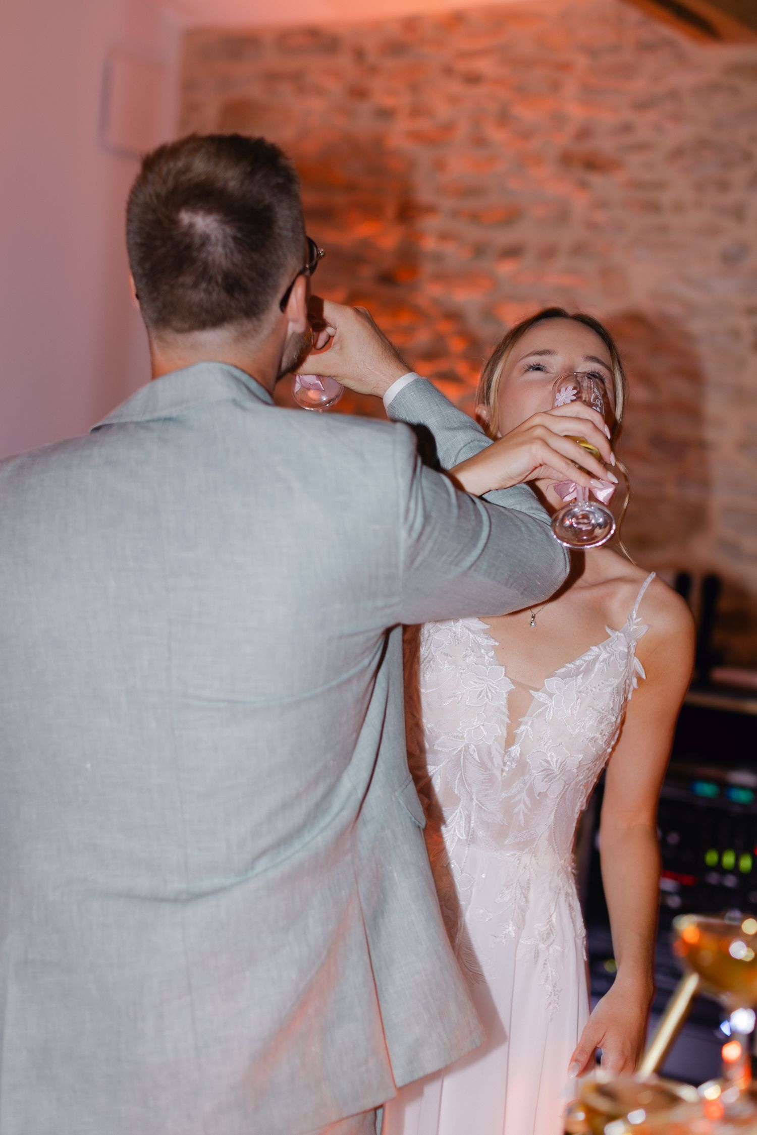 Marié en costume gris aidant la mariée en robe de mariée en dentelle blanche à boire du champagne à la réception de mariage.