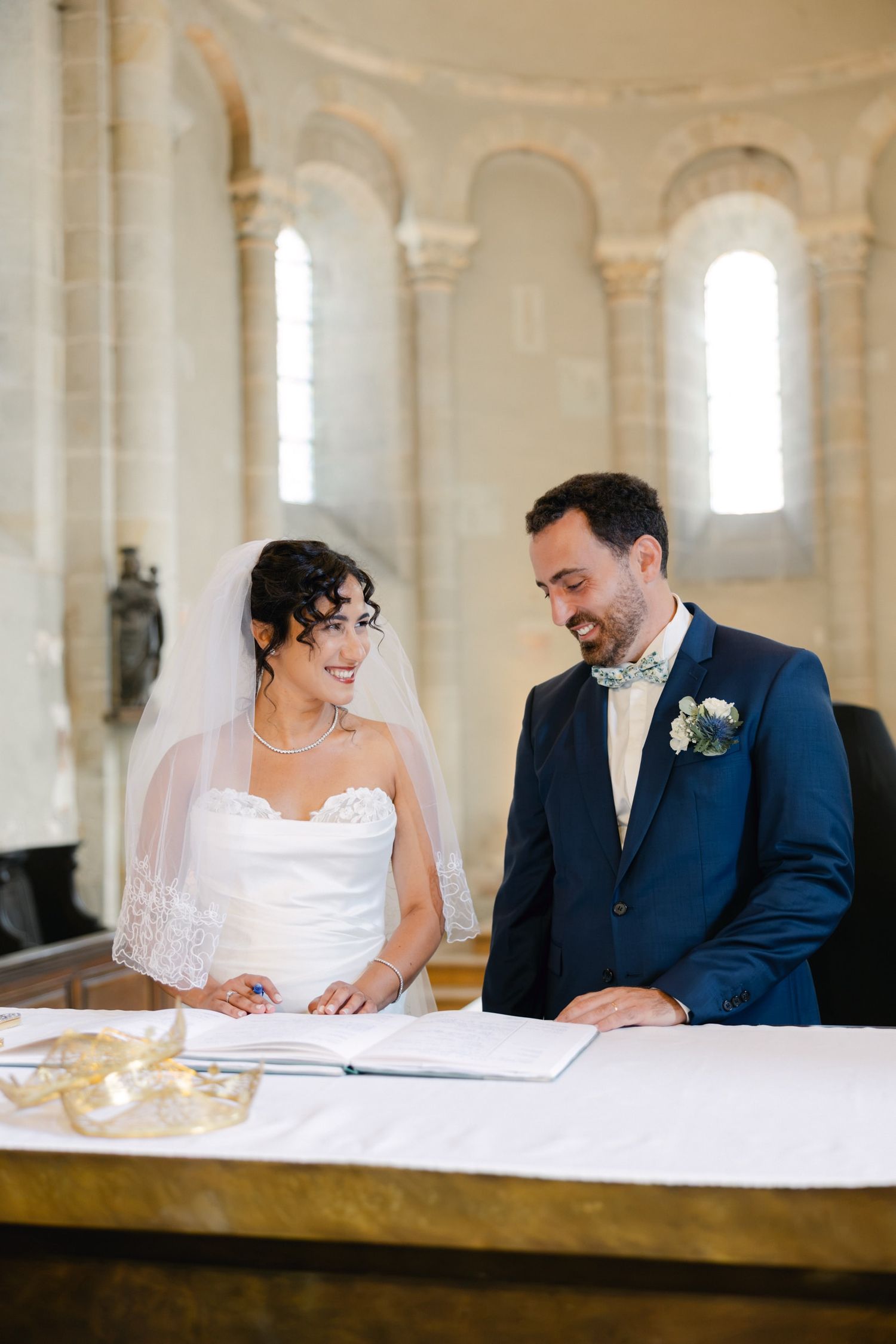 Bride and groom smiling while signing wedding register at church altar ceremony.