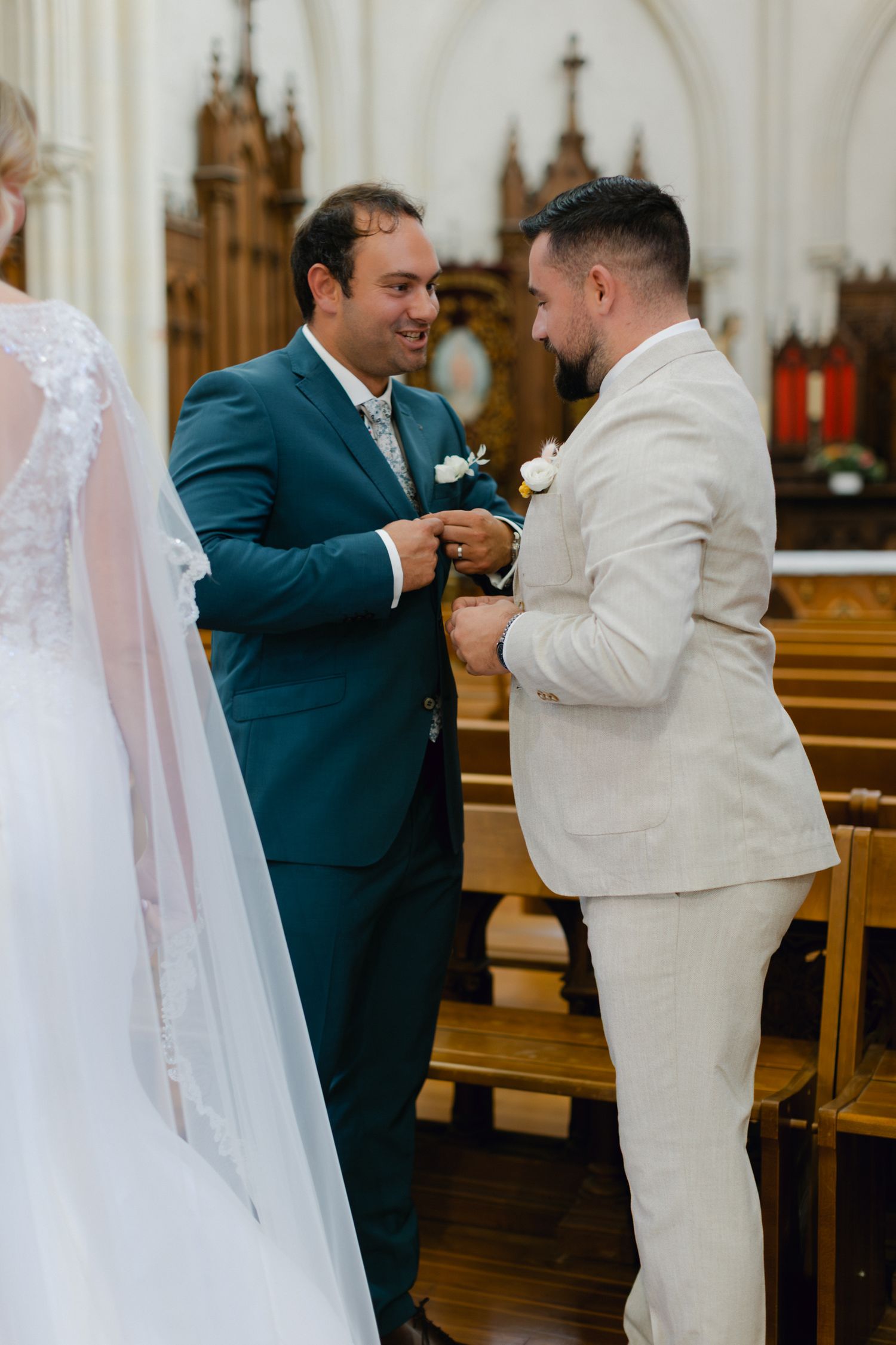 Le marié en costume sarcelle échange des bagues avec un témoin en costume beige lors de la cérémonie de mariage à l'église.