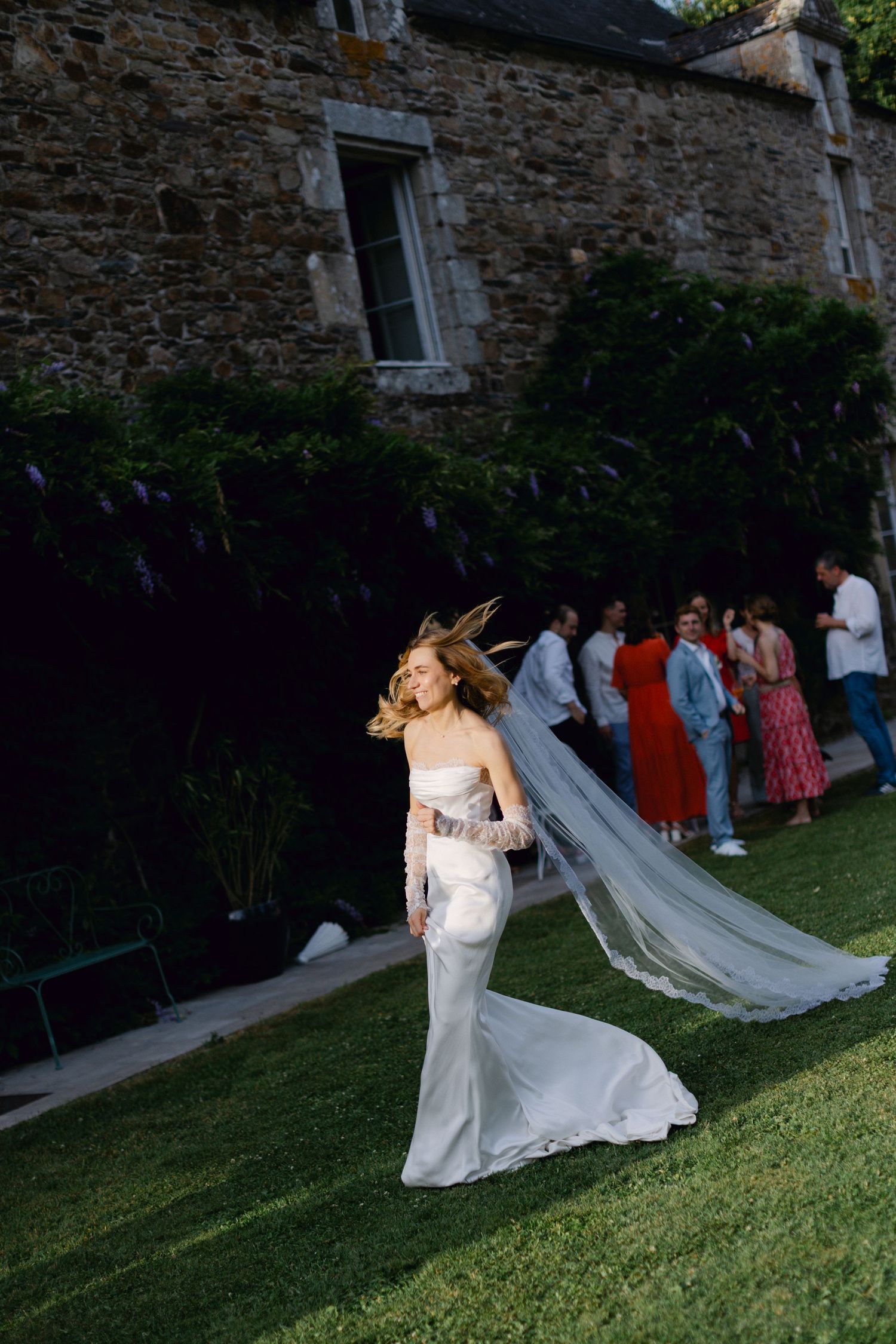 Une mariée vêtue d'une robe blanche avec un voile fluide marche gracieusement sur l'herbe verte.
