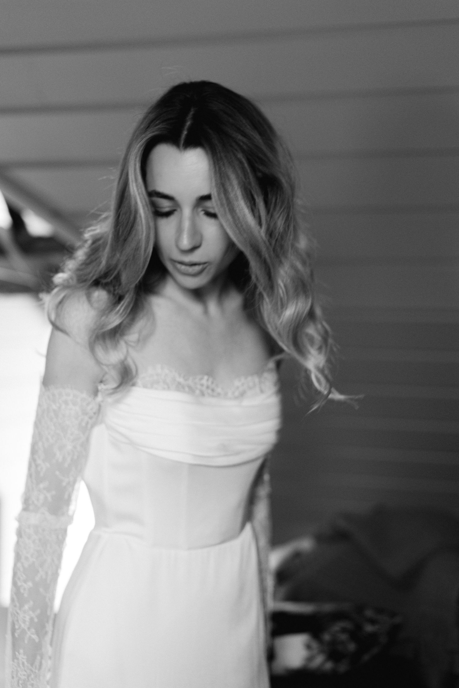 Portrait en noir et blanc d'une mariée vêtue d'une robe de mariée en dentelle à épaules dénudées avec des cheveux blonds fluides.