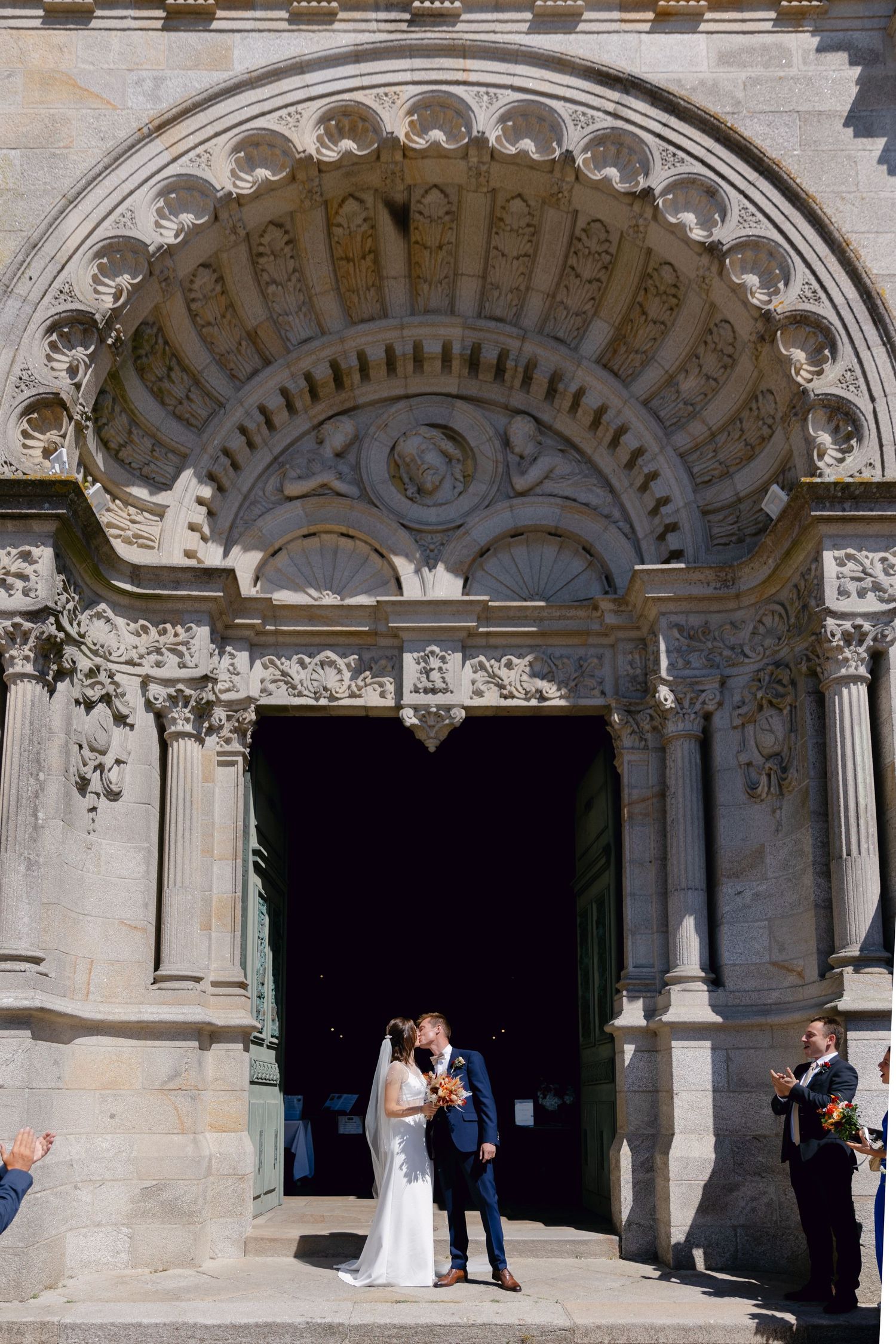 La mariée et le marié s'embrassent sous la porte en arc de pierre ornée de l'église historique le jour de leur mariage.