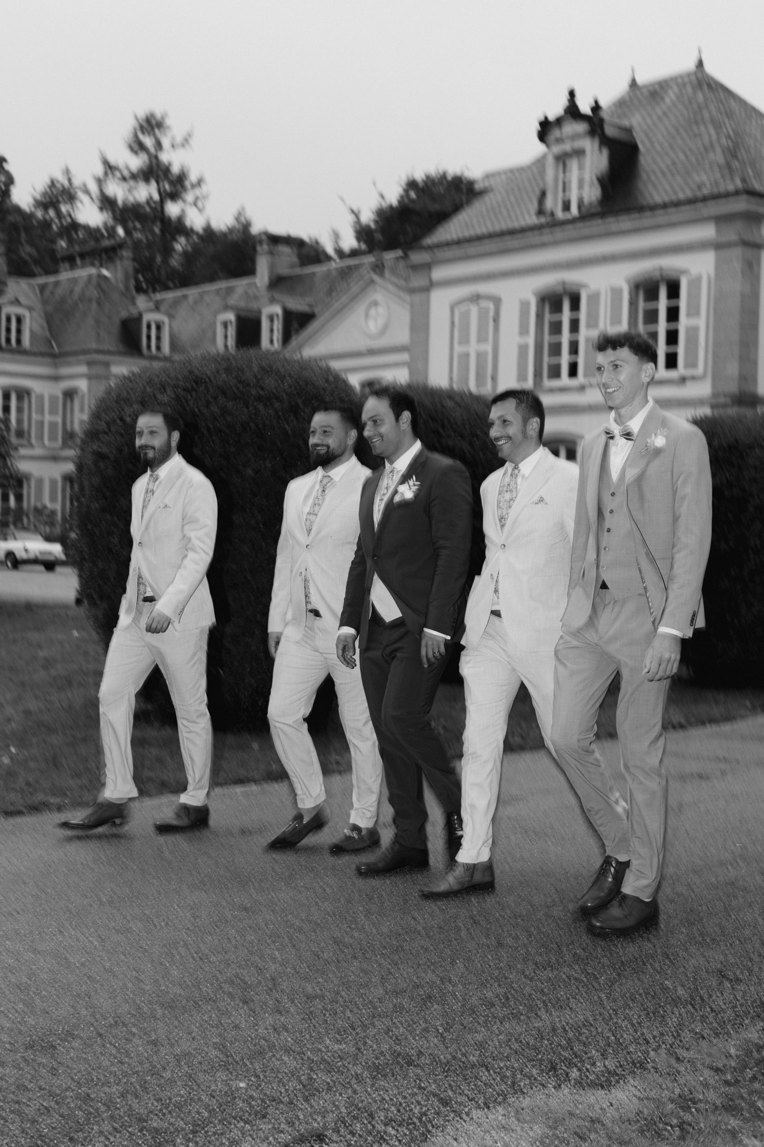 Photo en noir et blanc du marié et de quatre garçons d'honneur posant en costume à l'extérieur d'un élégant château.
