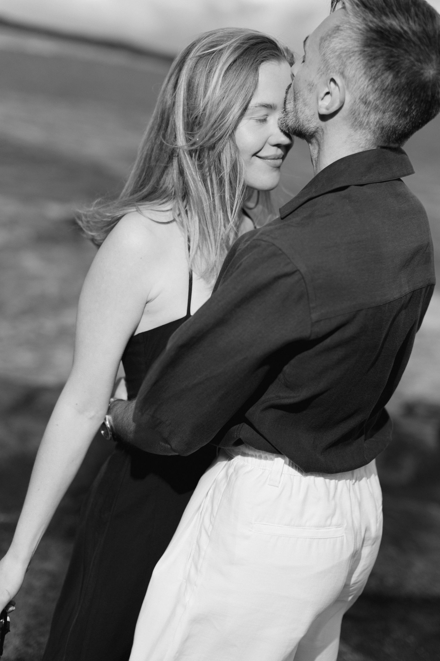 Photo en noir et blanc d'un couple partageant un tendre moment romantique, femme souriante les yeux fermés à l'extérieur.