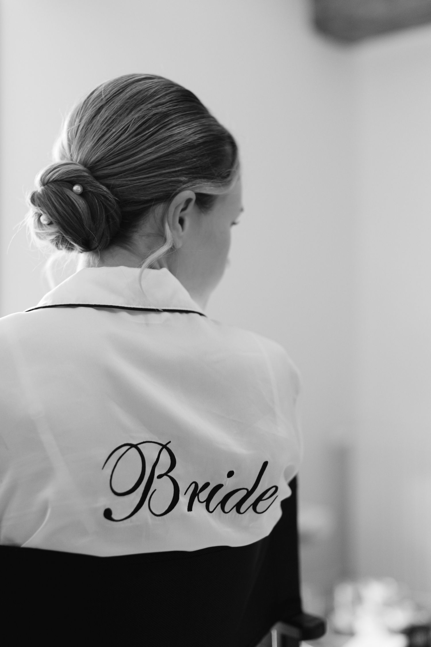 Mariée portant une robe en satin blanc avec texte cursive de la mariée, cheveux dans un élégant updo, photo en noir et blanc.