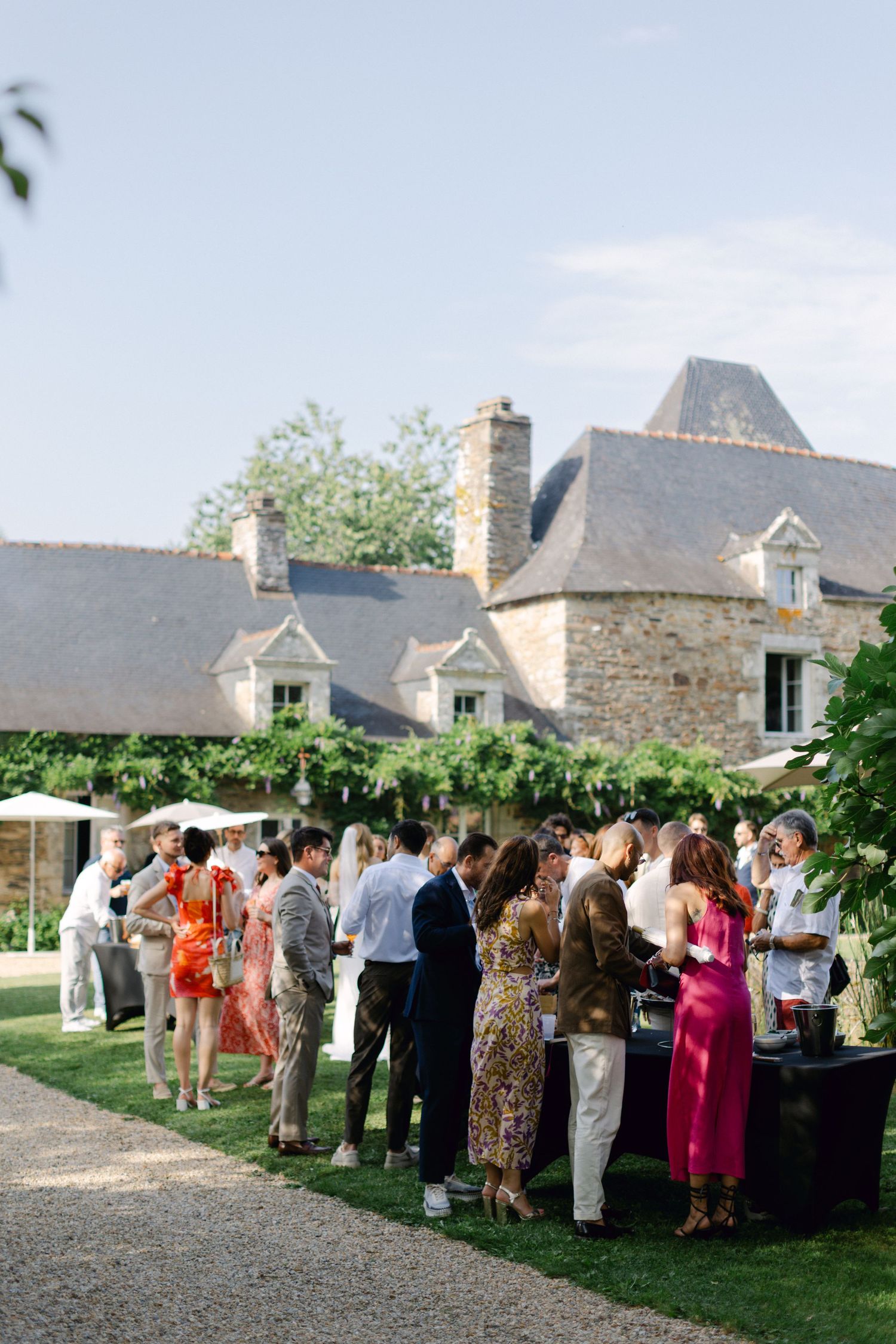 Les invités de mariage élégamment habillés se mêlent à l'extérieur à côté d'un charmant manoir français en pierre.