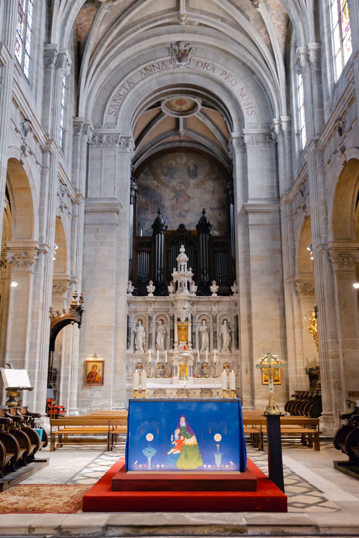 Intérieur d'une grande cathédrale avec un autel orné, un orgue à tuyaux et des œuvres d'art religieuses sous des arches voûtées en pierre.