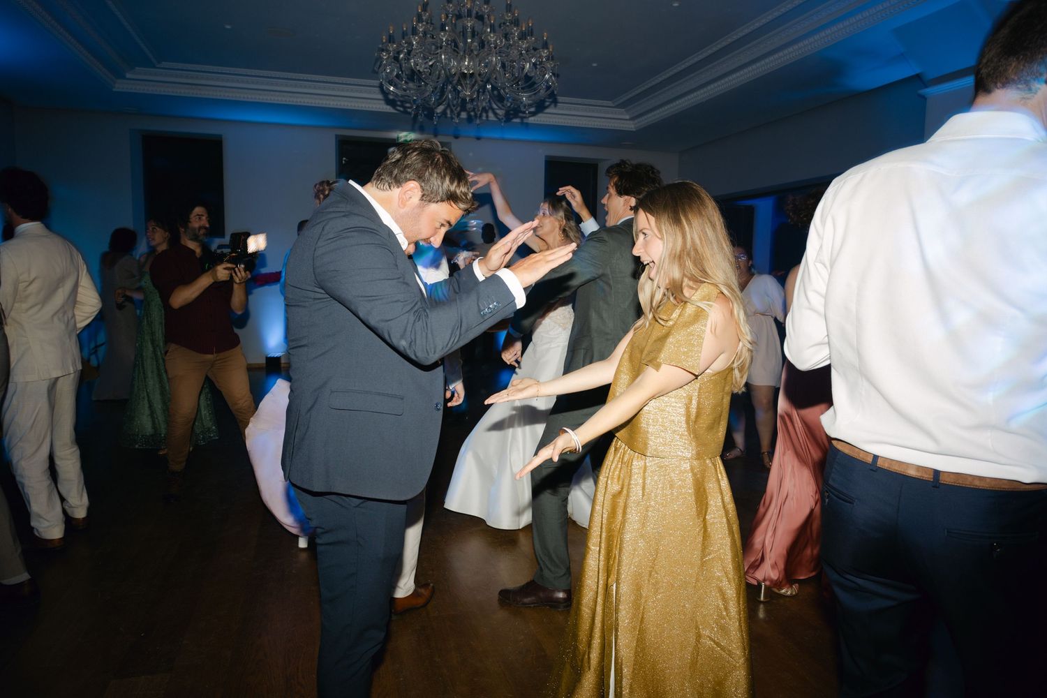 Des invités dansant ensemble lors d'une élégante réception de mariage sous un lustre avec un éclairage d'ambiance bleu.