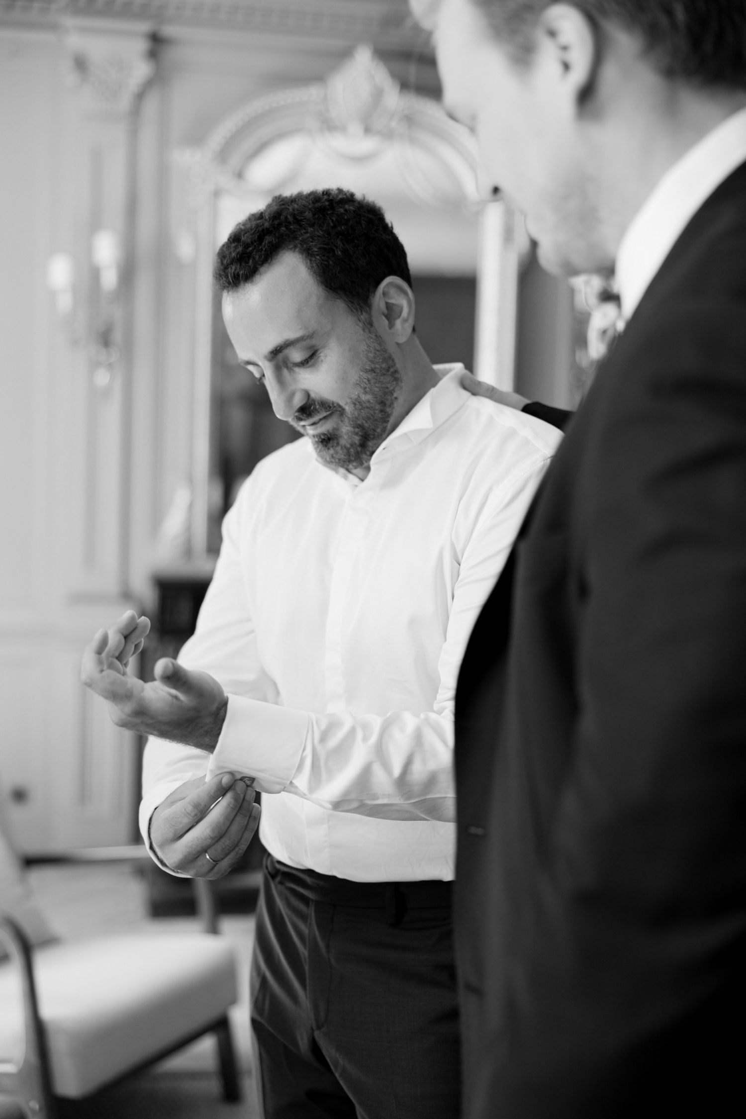Black and white photo of a man in a white dress shirt fastening his cufflinks before a formal event.