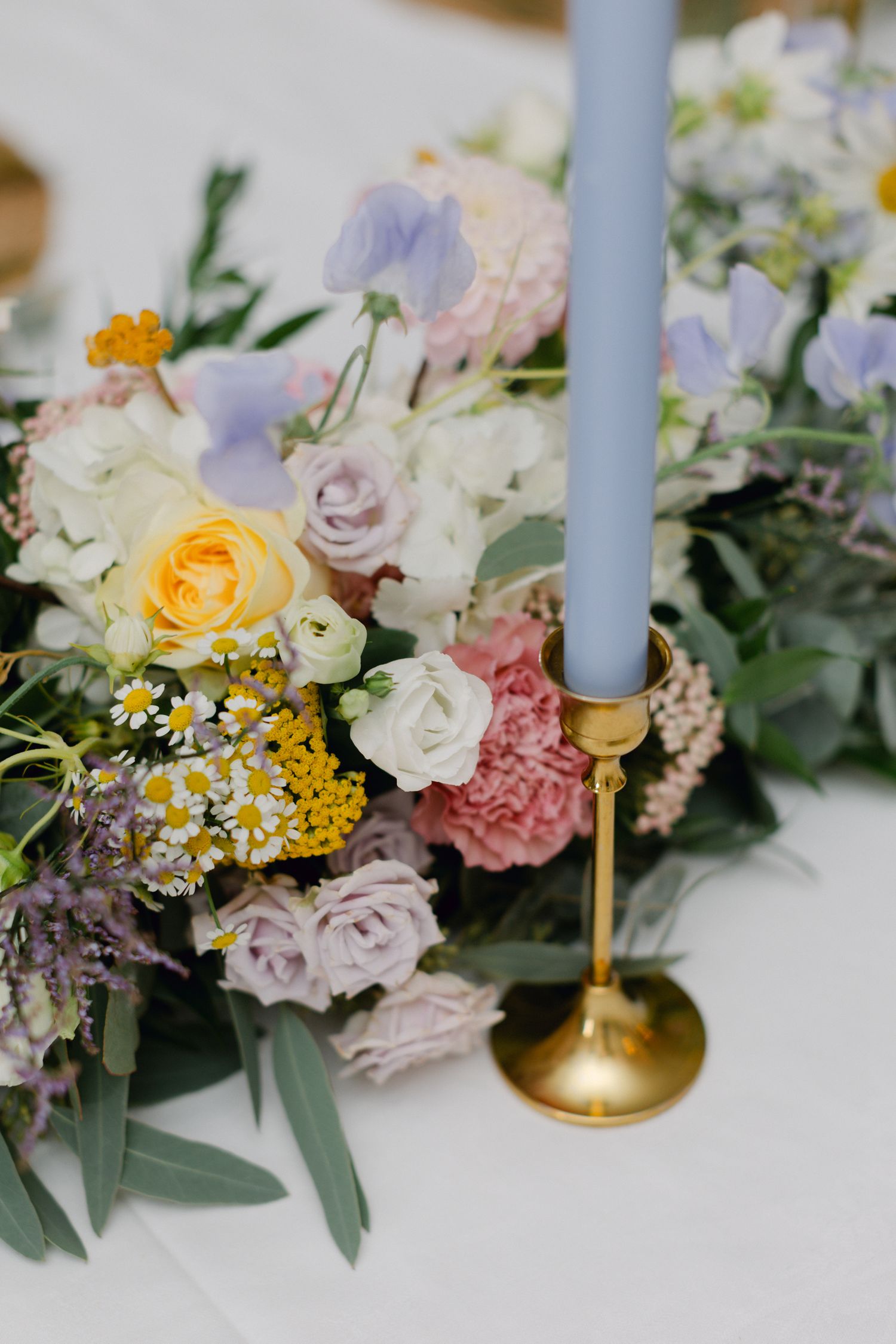 Centre de table de mariage avec roses pastel, bougie conique bleue dans un bougeoir doré.