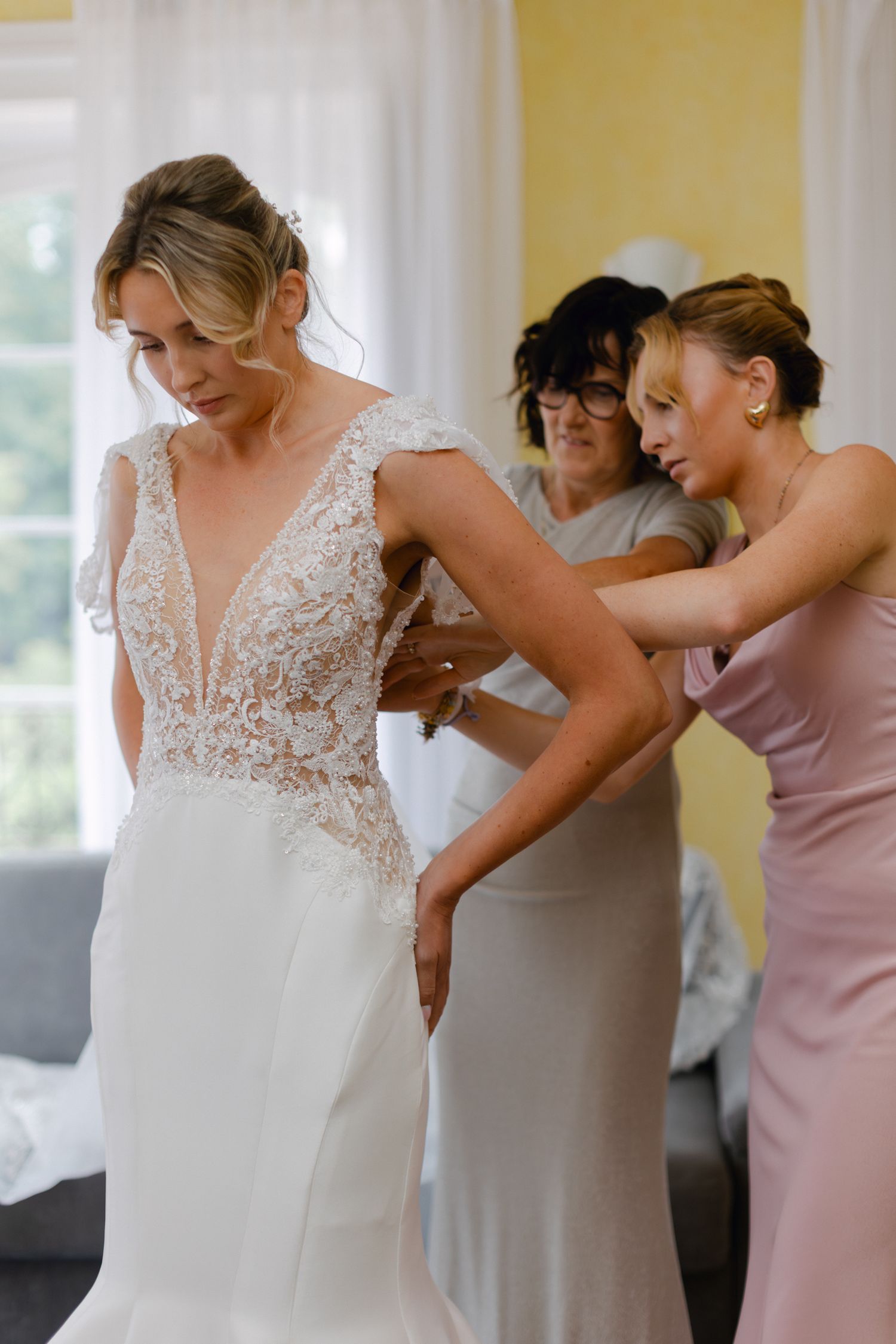 Les demoiselles d'honneur aident la mariée dans une élégante robe de mariée en dentelle à col en V avec des manches courtes dans une chambre