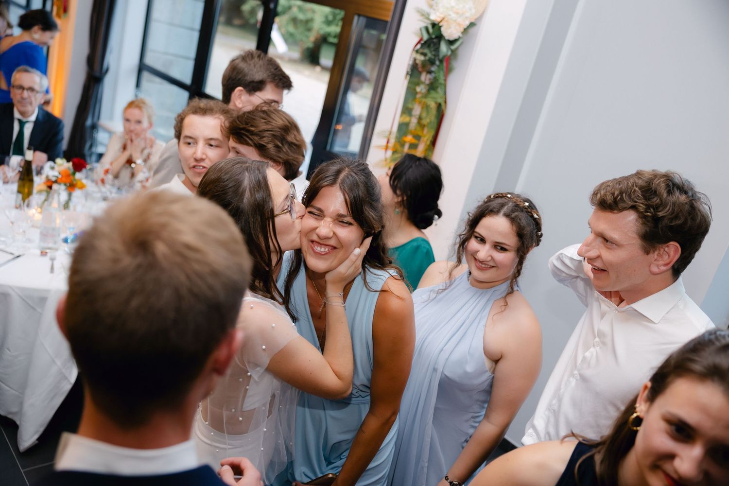 Des invités socialisant et riant lors d'une réception de mariage, portant une tenue formelle dans un lieu lumineux et élégant.