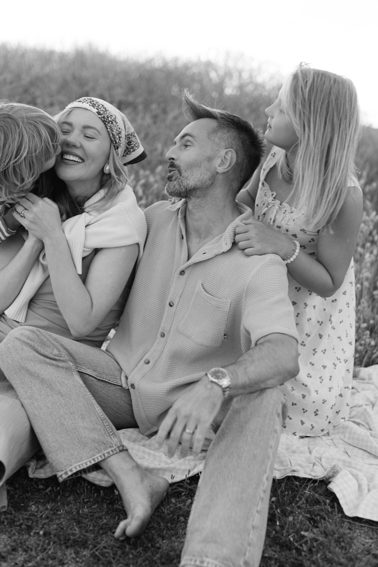 Black and white family photo of parents and two young daughters sharing a joyful moment outdoors.