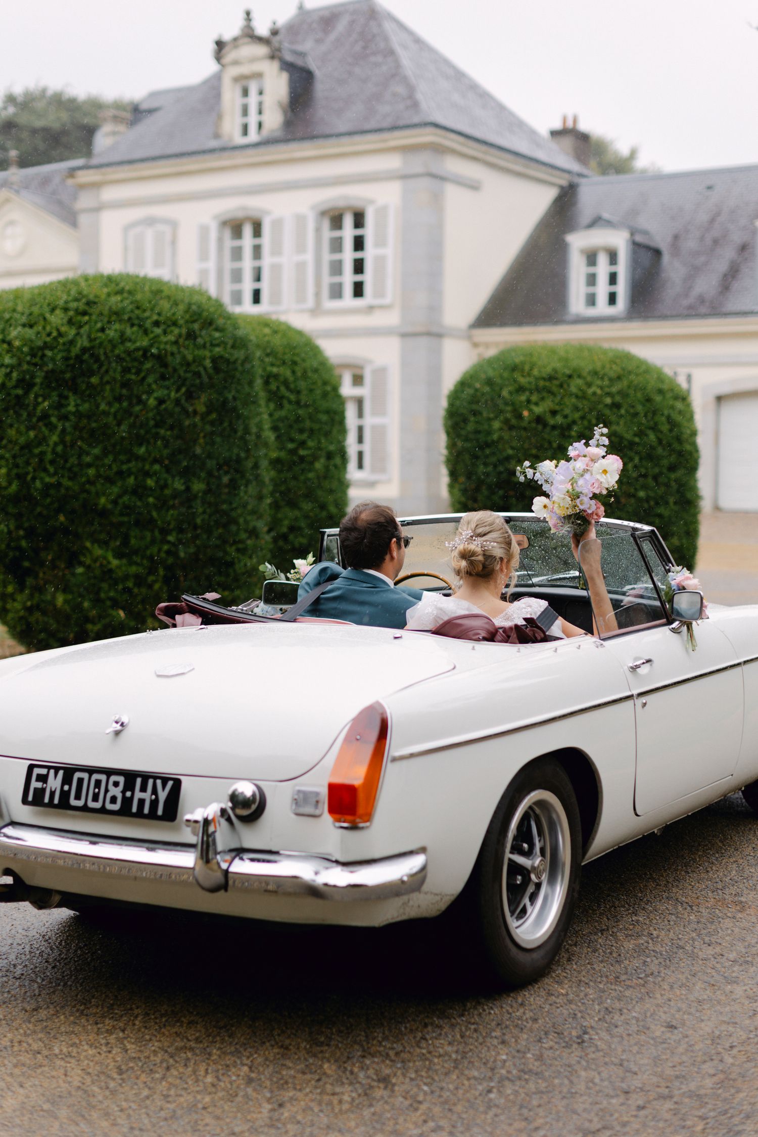 La mariée et le marié partent dans un décapotable MG blanc classique après le lieu de mariage du château français.