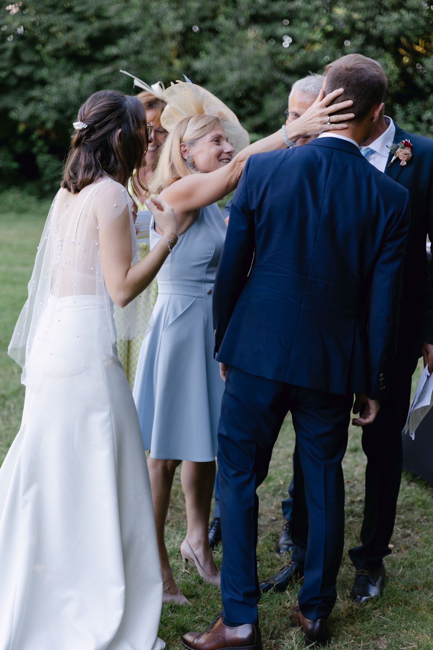 Les invités à la fête de mariage félicitant la mariée et le marié à l'extérieur, une femme au chapeau jaune embrassant un couple dans un jar