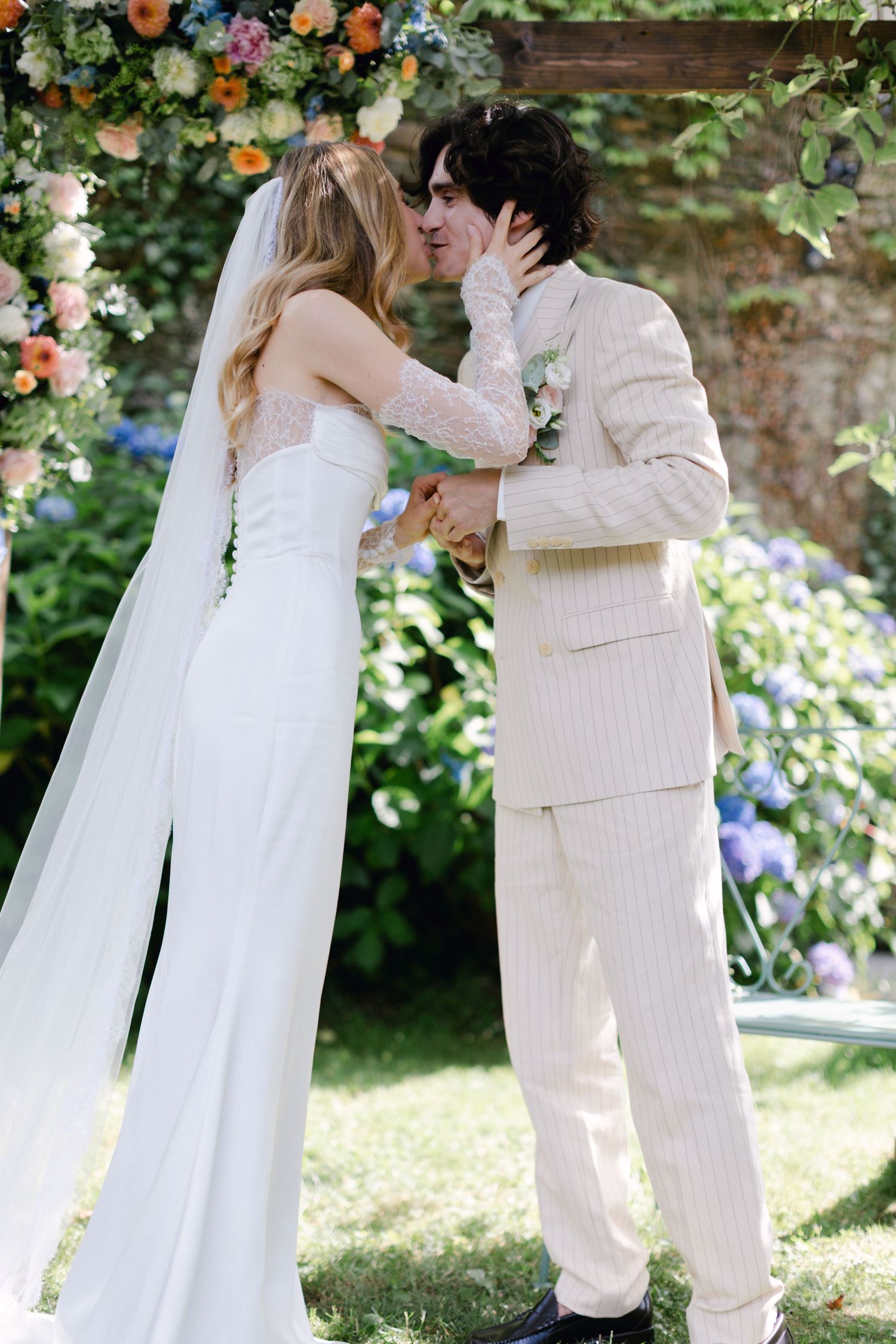 La mariée et le marié partagent le premier baiser sous une arche florale lors d'une cérémonie de mariage dans le jardin en plein air.