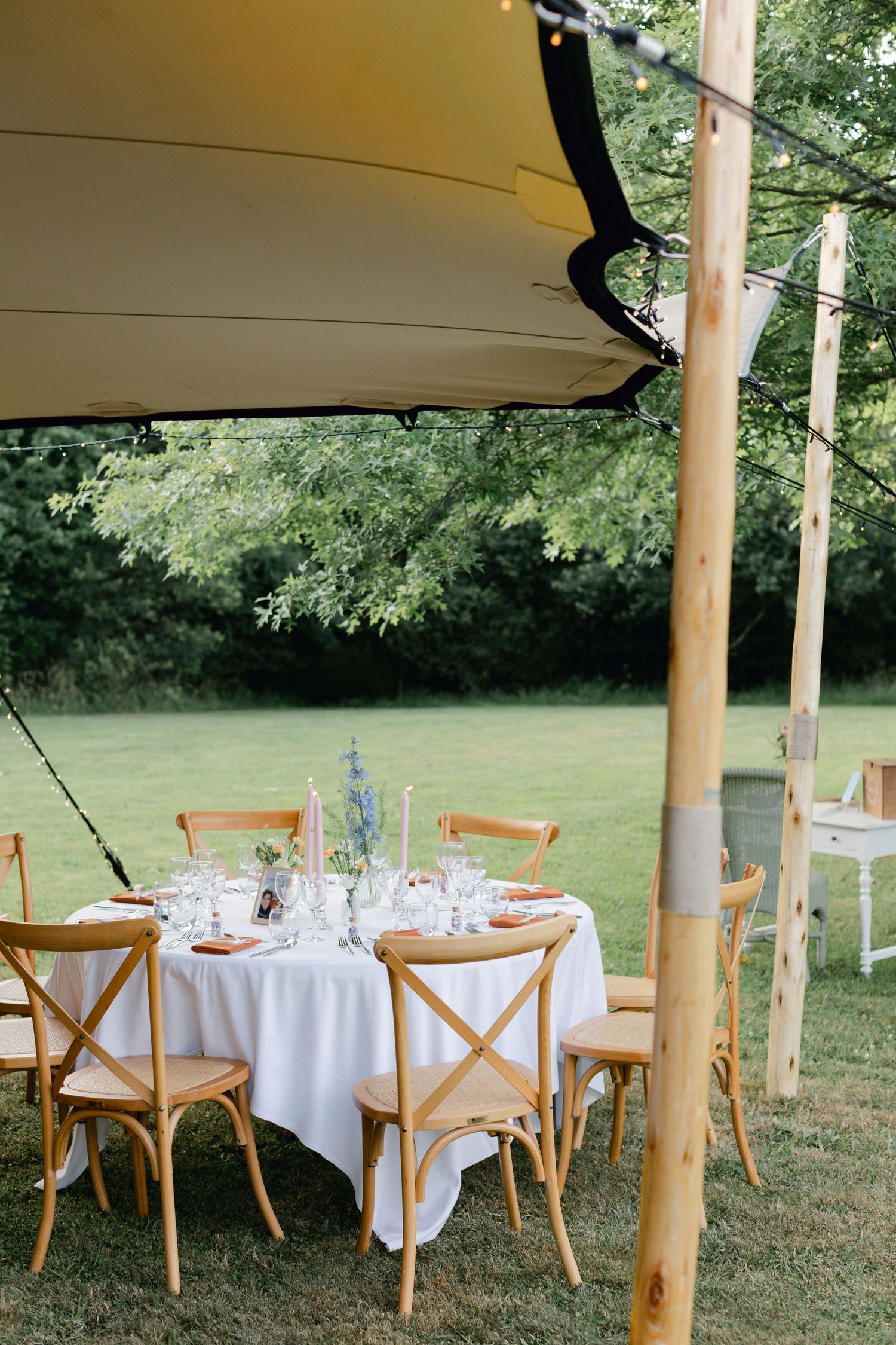 Réception de mariage en plein air sous une tente extensible avec des chaises en bois à dossier croisé et des tables rondes.
