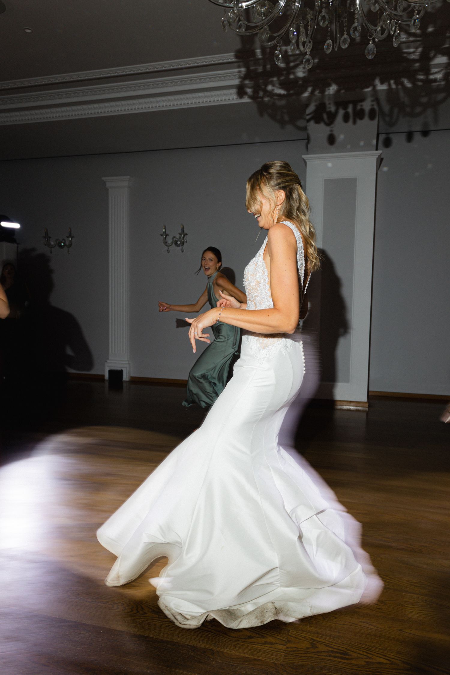 Mariée tourbillonnant dans une superbe robe de mariée sirène blanche sur la piste de danse sous un lustre en cristal.