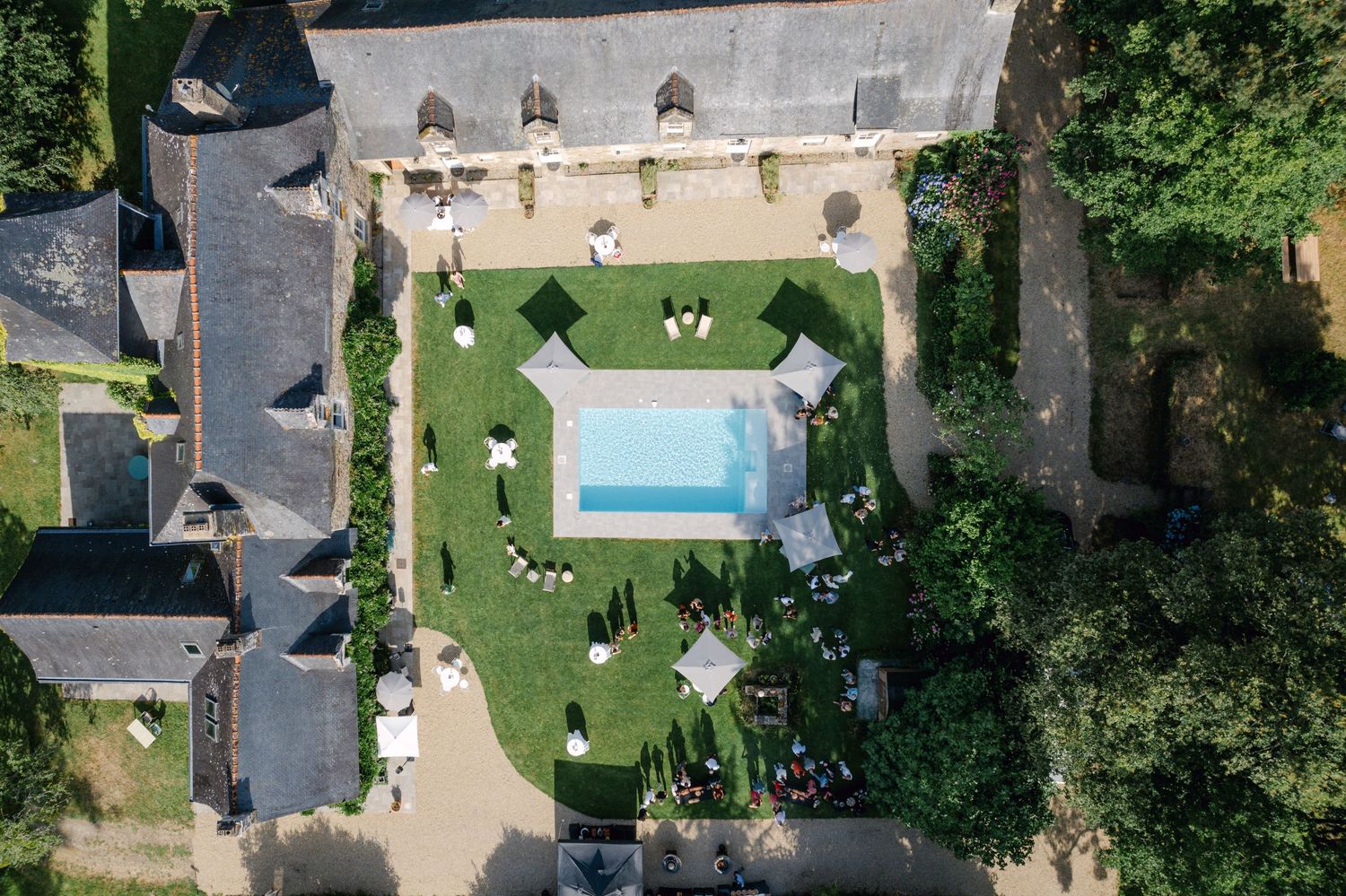 Vue aérienne d'un domaine en pierre française avec une piscine rectangulaire entourée de jardins bien entretenus.
