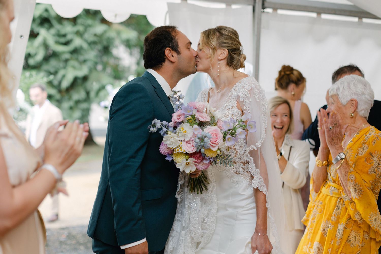 Les jeunes mariés partagent leur premier baiser sous la tente tandis que les invités applaudissent lors de la cérémonie de mariage française