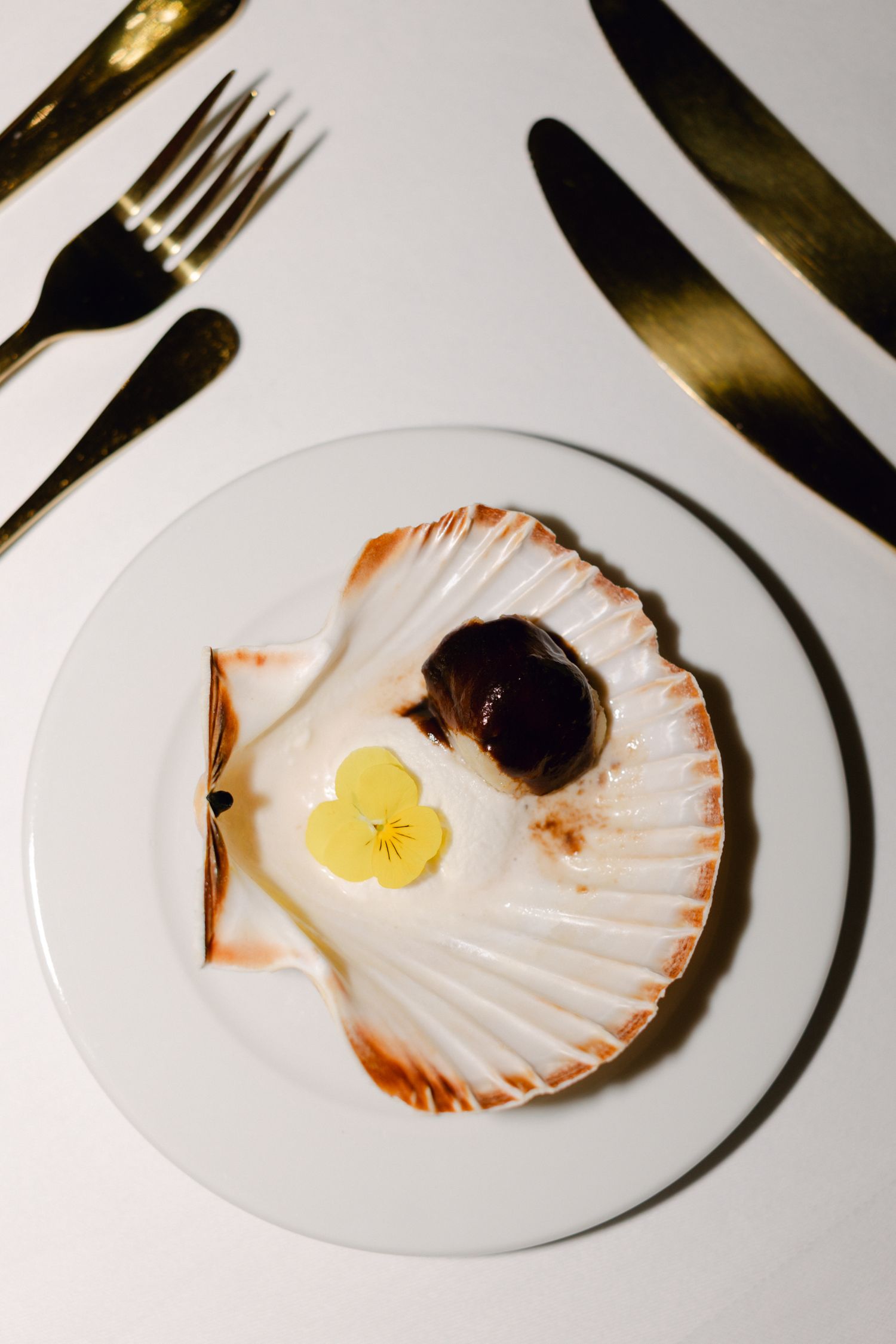 Apéritif de mariage élégant servi en coquille Saint-Jacques avec fleur comestible sur assiette blanche avec couverts en or.