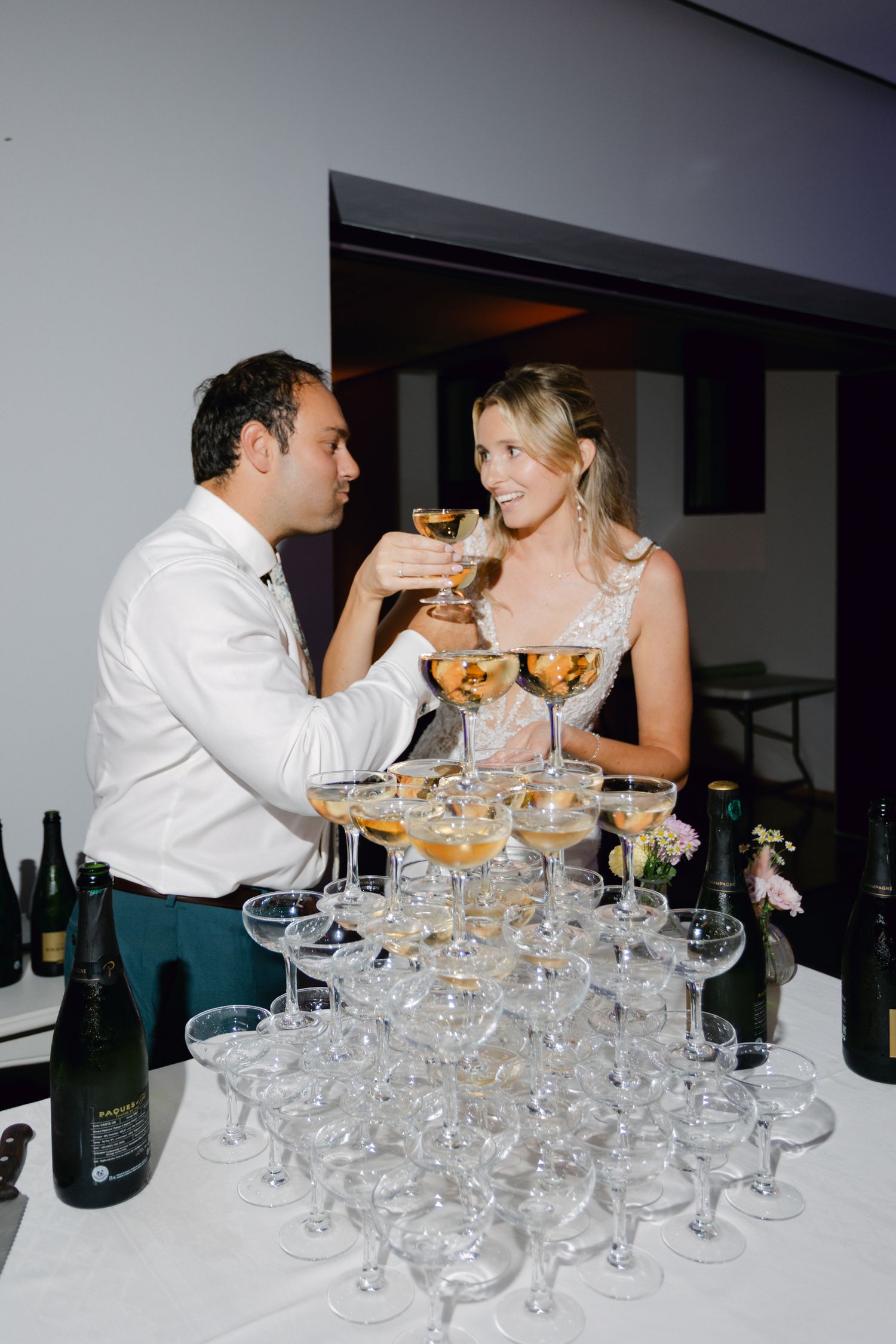 La mariée et le marié tintant des verres de coupé à champagne à côté d'une grande tour de champagne lors de la réception de mariage.