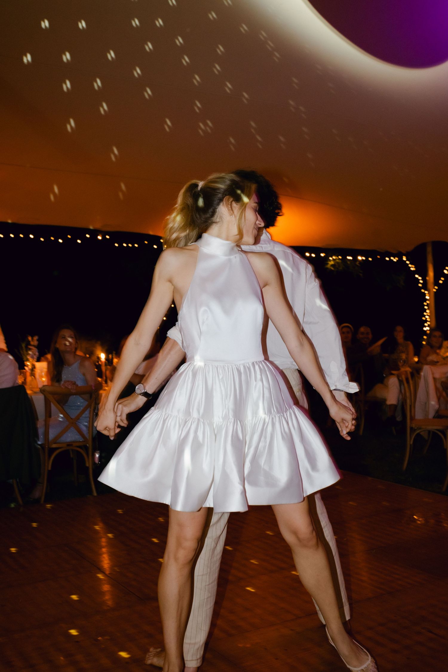 Mariée en mini-robe blanche dansant énergiquement sous les lumières de la boule disco lors de la réception de mariage.
