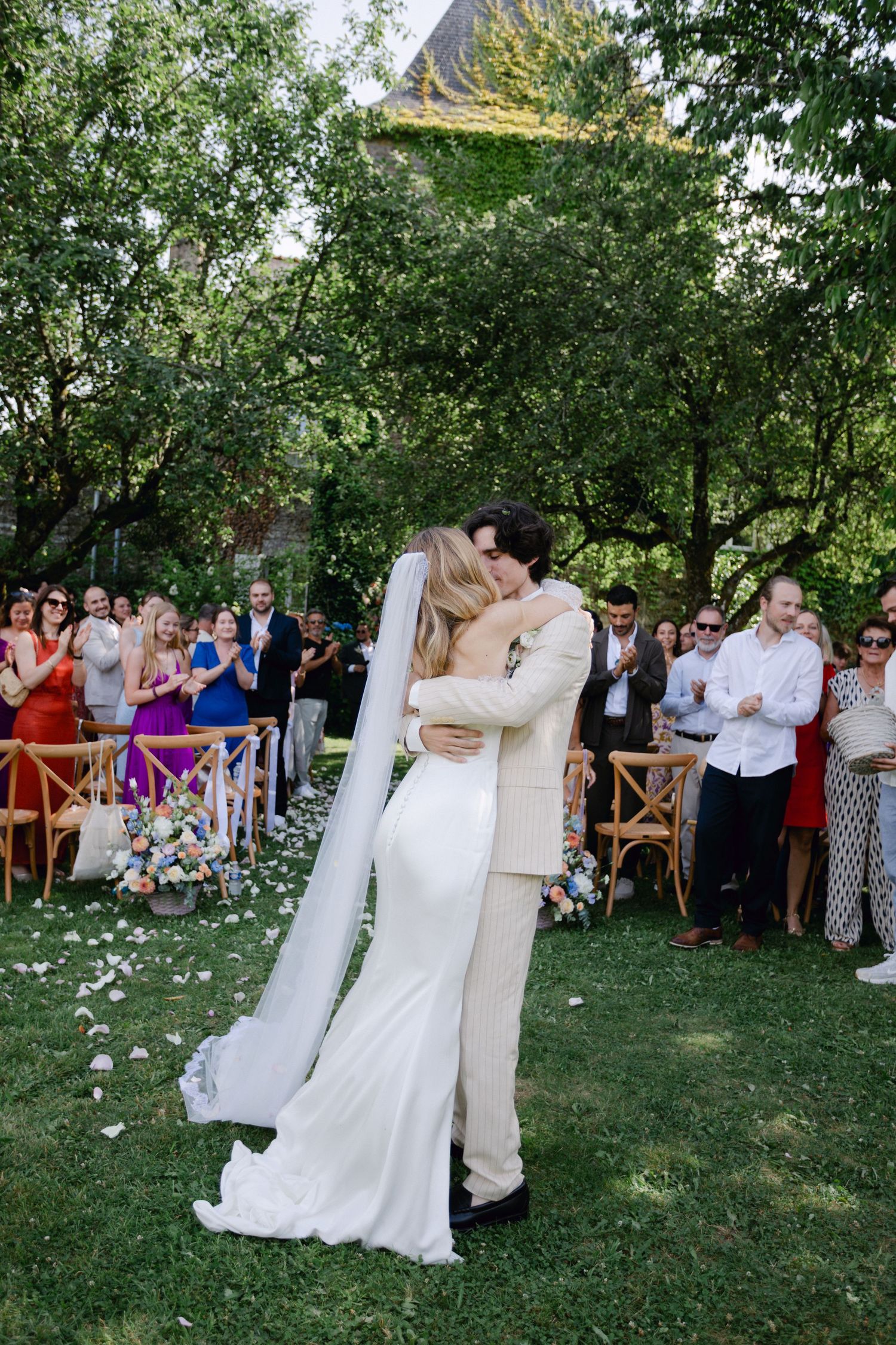 Les jeunes mariés partagent un baiser romantique tandis que les invités applaudissent lors d'un mariage luxuriant dans un jardin vert récess