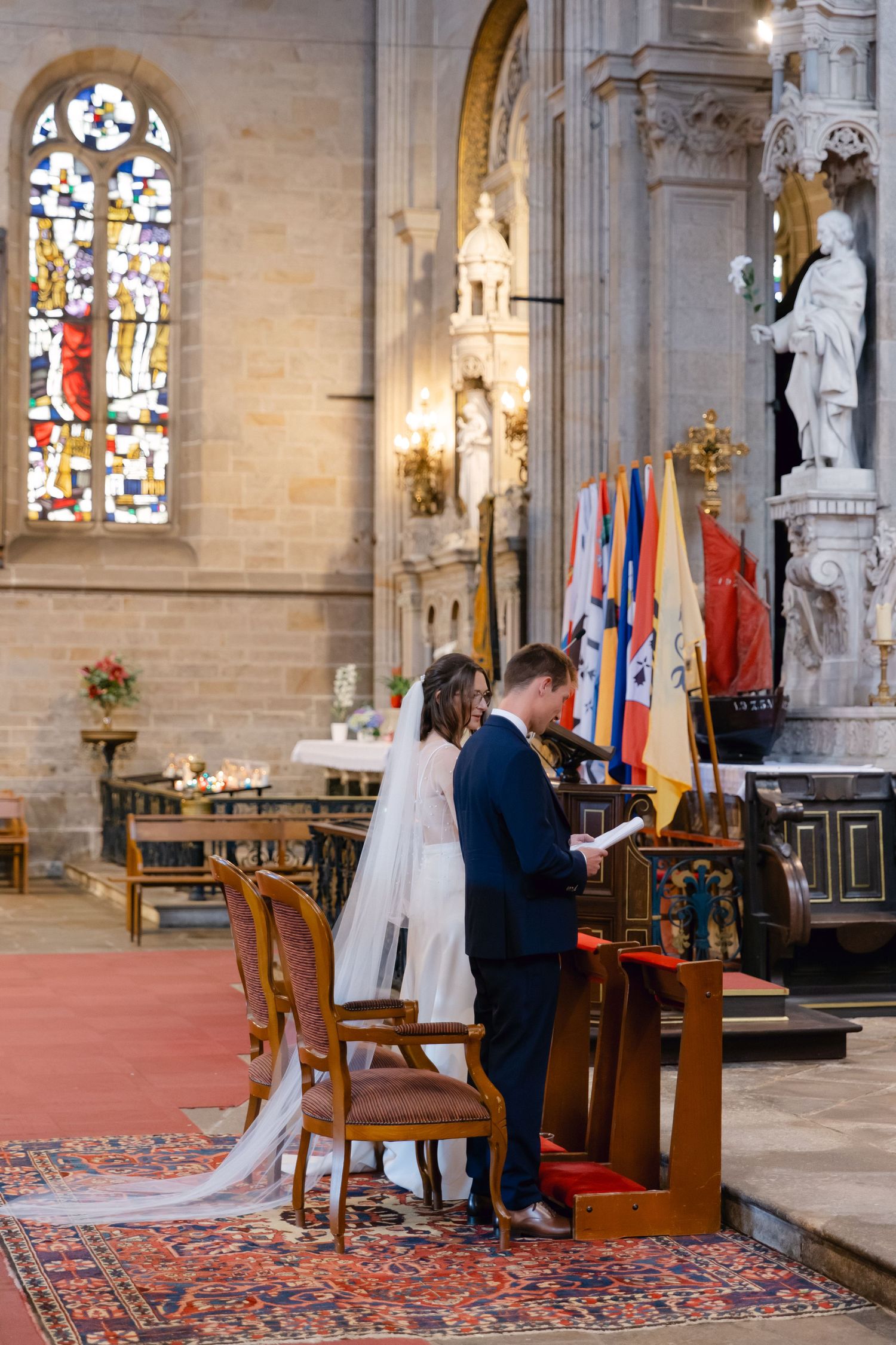 Mariée et marié échangeant des vœux à l'autel de l'église orné lors de la cérémonie de mariage avec des vitraux.