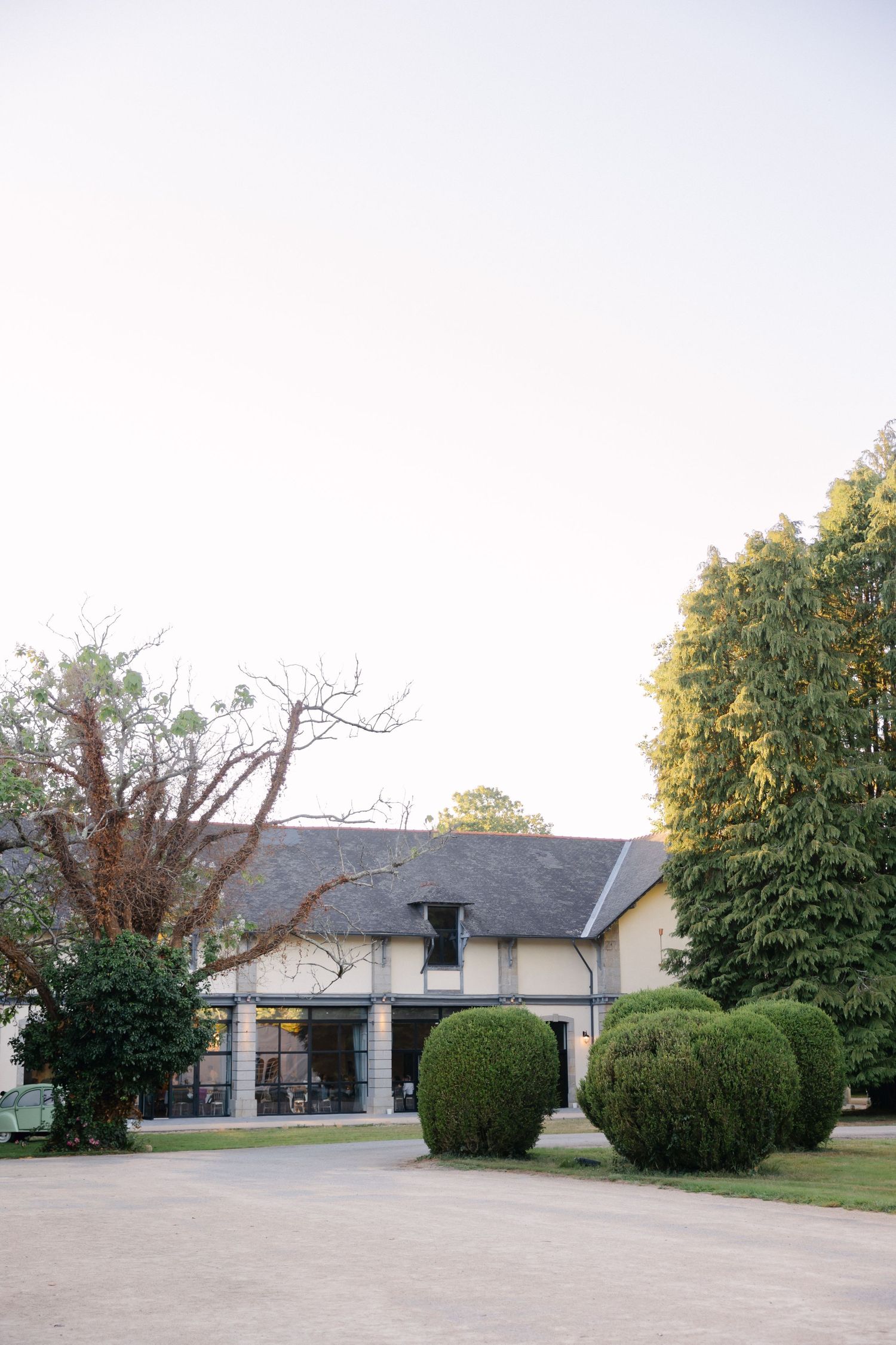 Bâtiment colonial de deux étages avec des haies bien entretenues et de grands arbres dans une cour spacieuse au crépuscule.