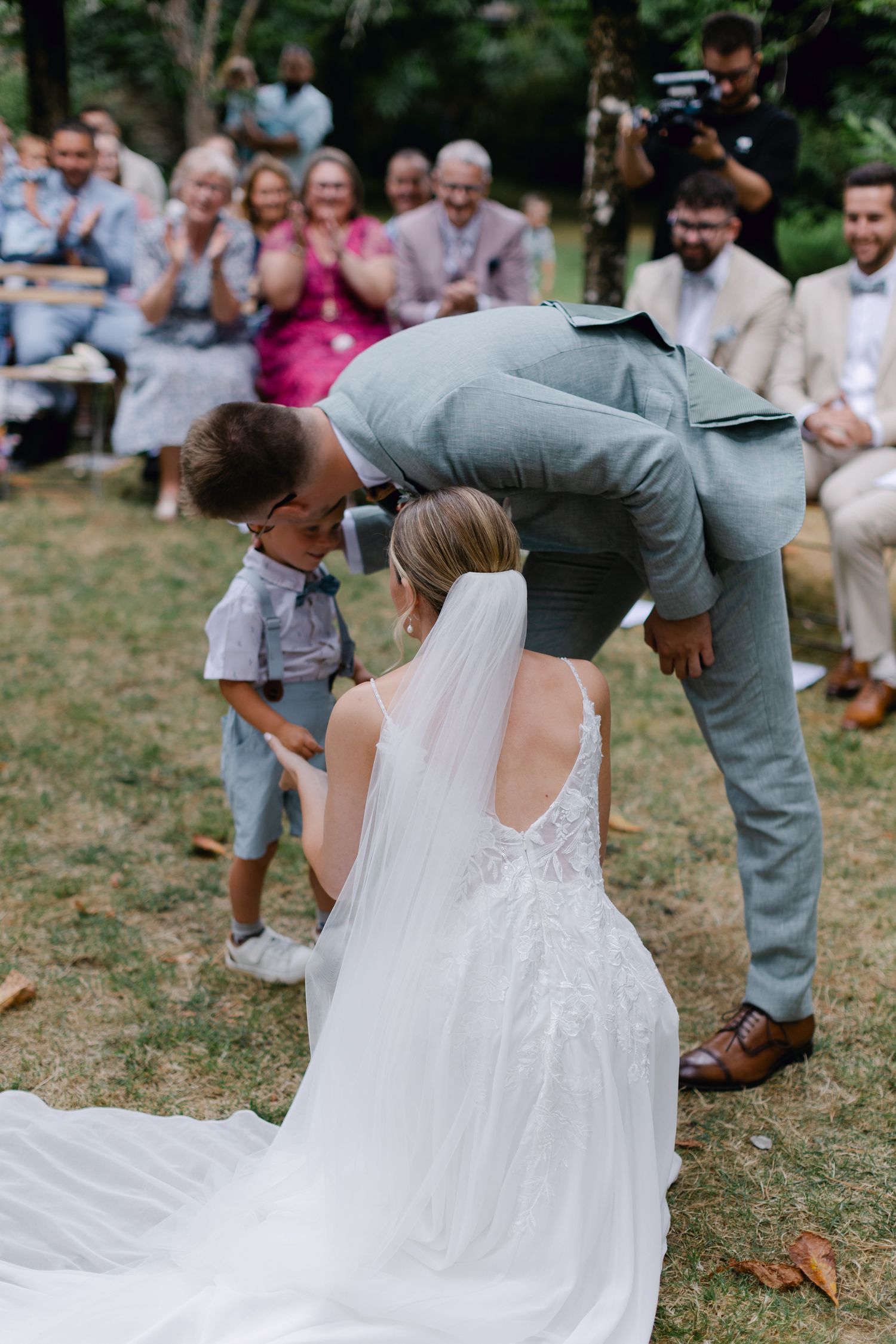 Le marié se penche pour saluer un jeune enfant pendant que la mariée est assise lors de la cérémonie de mariage en plein air.